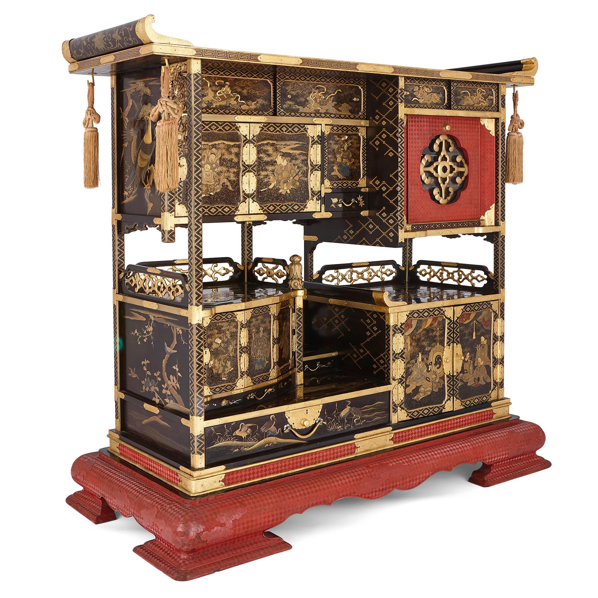 This black lacquer kazaridana (display cabinet) was crafted in the Meiji period in Japan. The body of the cabinet is topped by a roof with upward-curving ends, which faded red tassels hang from. The cabinet is divided in half lengthways by a gap in