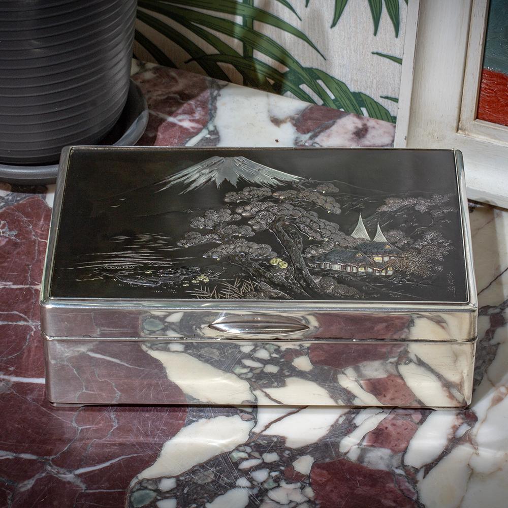 De nuestra colección japonesa, nos complace presentar esta Caja Japonesa de Plata y Metales Mixtos de Hidekuni. Caja japonesa de gran forma rectangular forrada de madera noble oscura de tipo palisandro asiático montada en plata pura japonesa con la