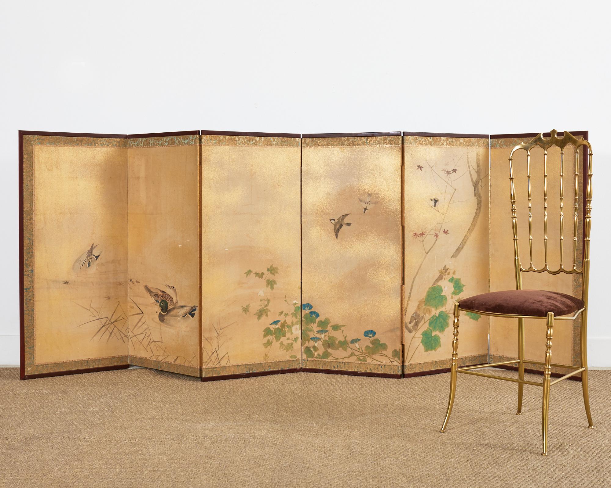 19th century Japanese Meiji period six-panel screen depicting a serene water landscape with ducks and songbirds amid Momiji (red maple) hibiscus, and morning glory. Made in the Nihonga school style decorated with gold flecks. Beautifully crafted