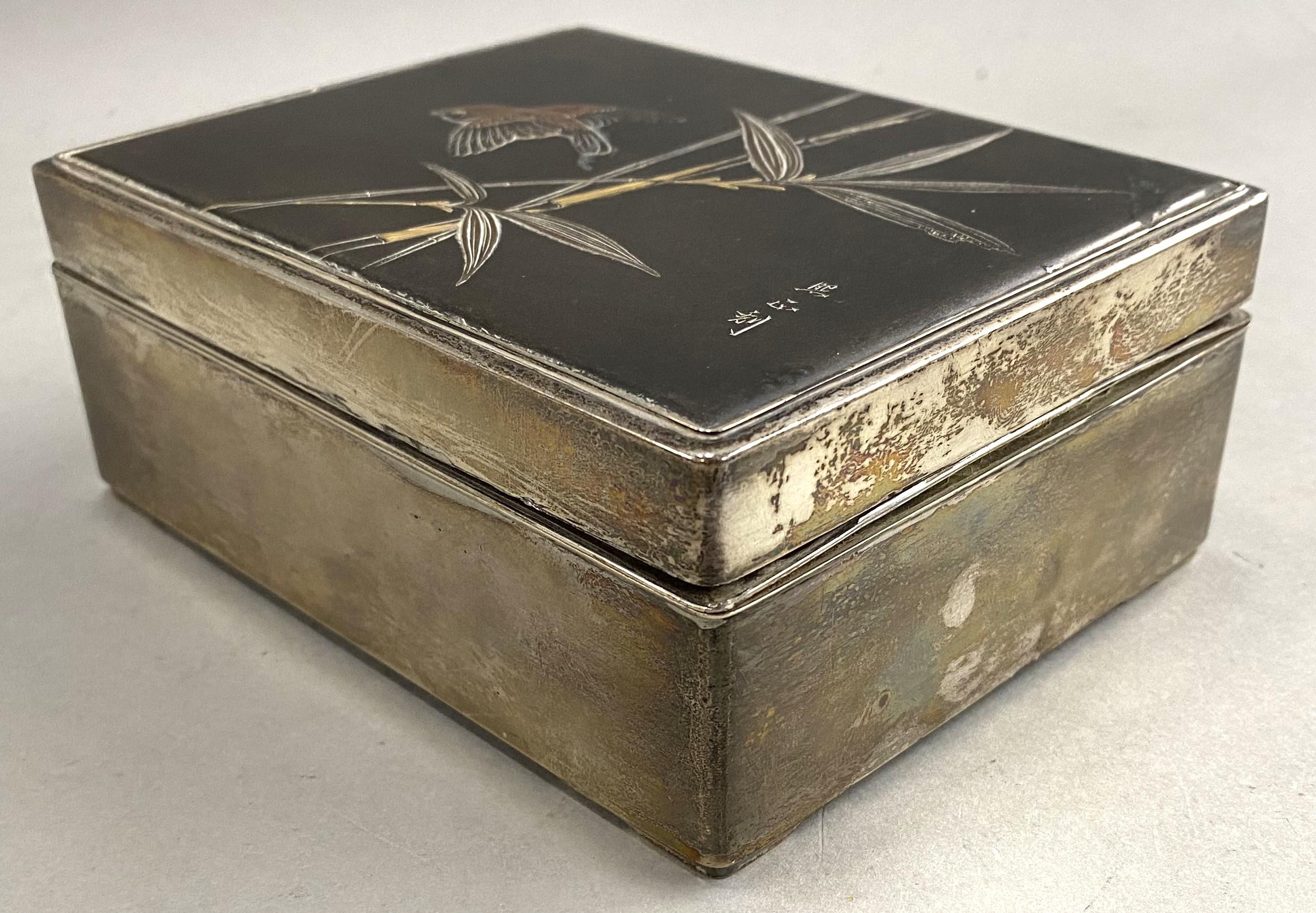 A fine Japanese Meiji silver and mixed metal cigarette box with bird and foliate decoration on the cover, signed on cover, and ebonized wooden interior, dating to the late 19th/early 20th century in very good overall condition, with slight tarnish