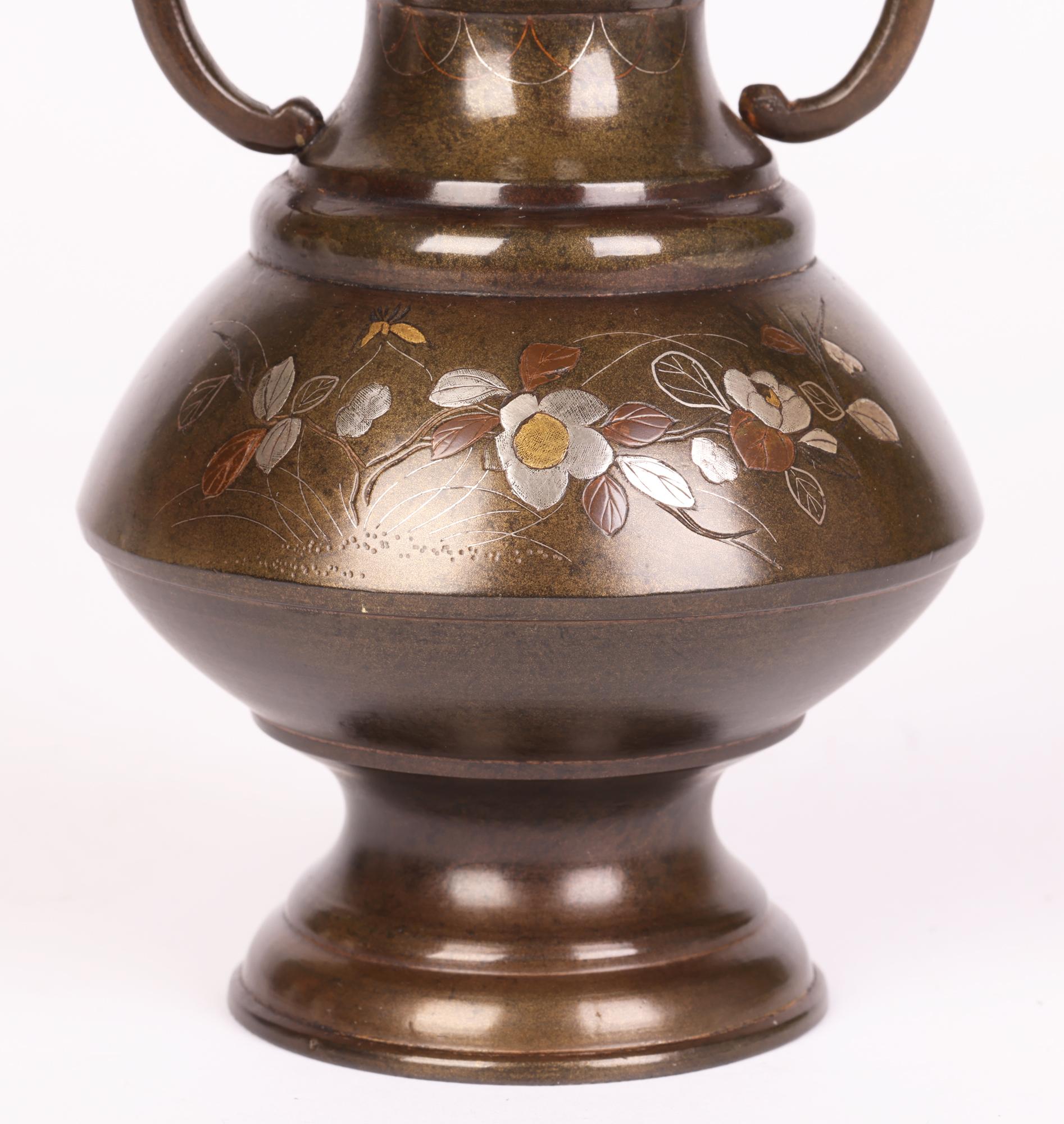 A fine antique Japanese Meiji twin handled bronze vase decorated with floral designs in silver, brass and copper inlay dating from the 19th century. The vase stands raised on a round pedestal foot with narrow stem and shaped round lower body with a