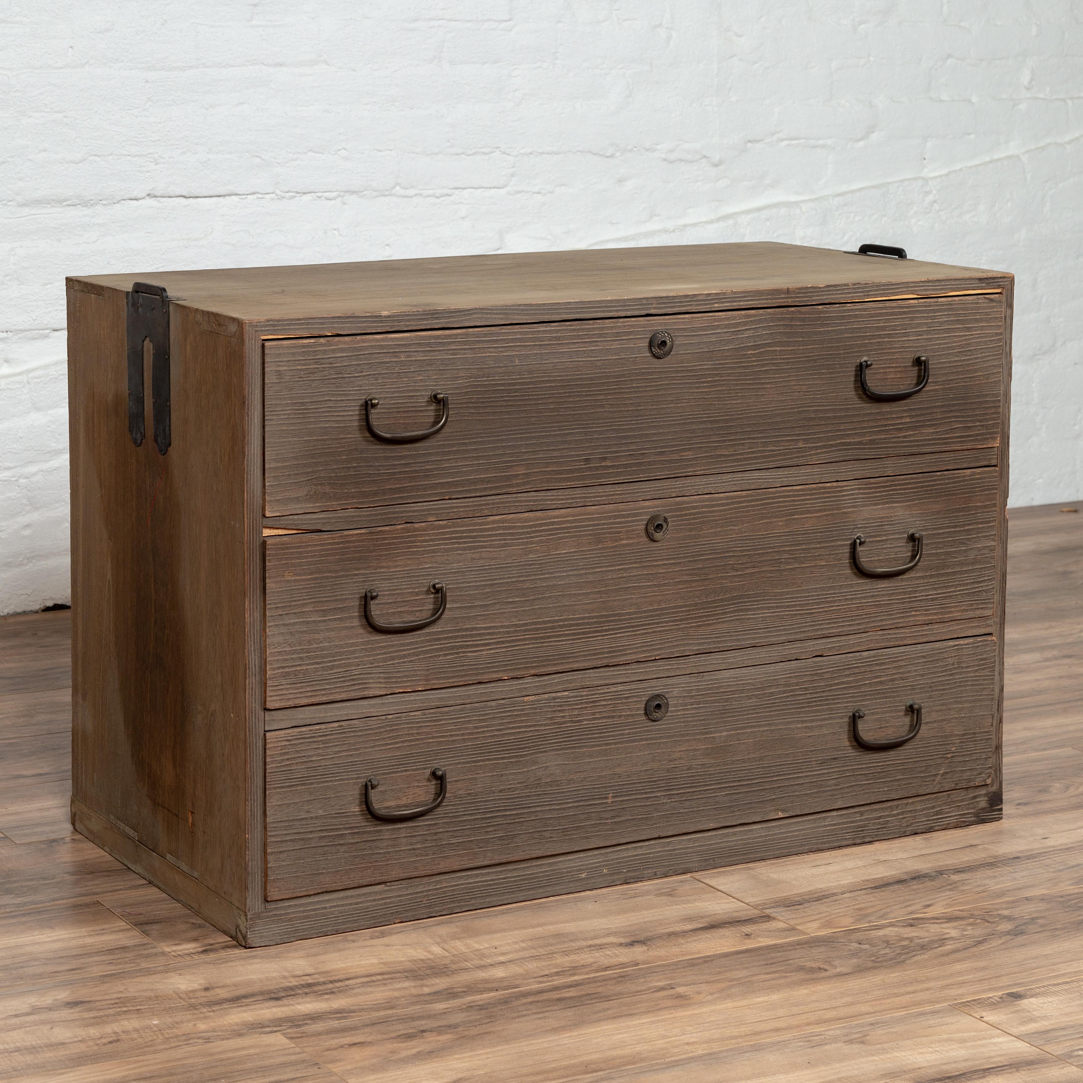 An antique Japanese Meiji period tansu chest from the 19th century, with three drawers, carrying handles and greyish patina. Born in Japan during the Meiji period, this tansu traveling chest-of-drawers features a rectangular top sitting above three
