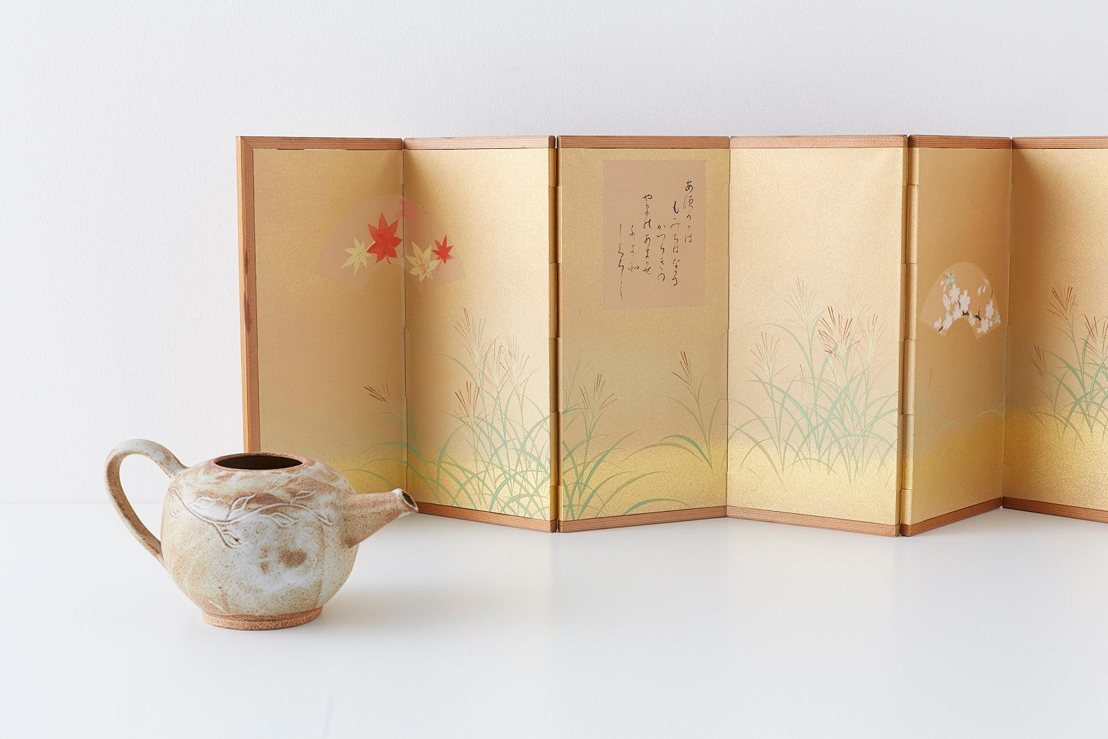 Dimmutive Japanese six-panel autumn screen depicting delicate flowers and grasses. Miniature table screen decorated with gilt sprays and floral fans on each side centered by a classical Japanese waka poem in cursive script. Set in a natural pine