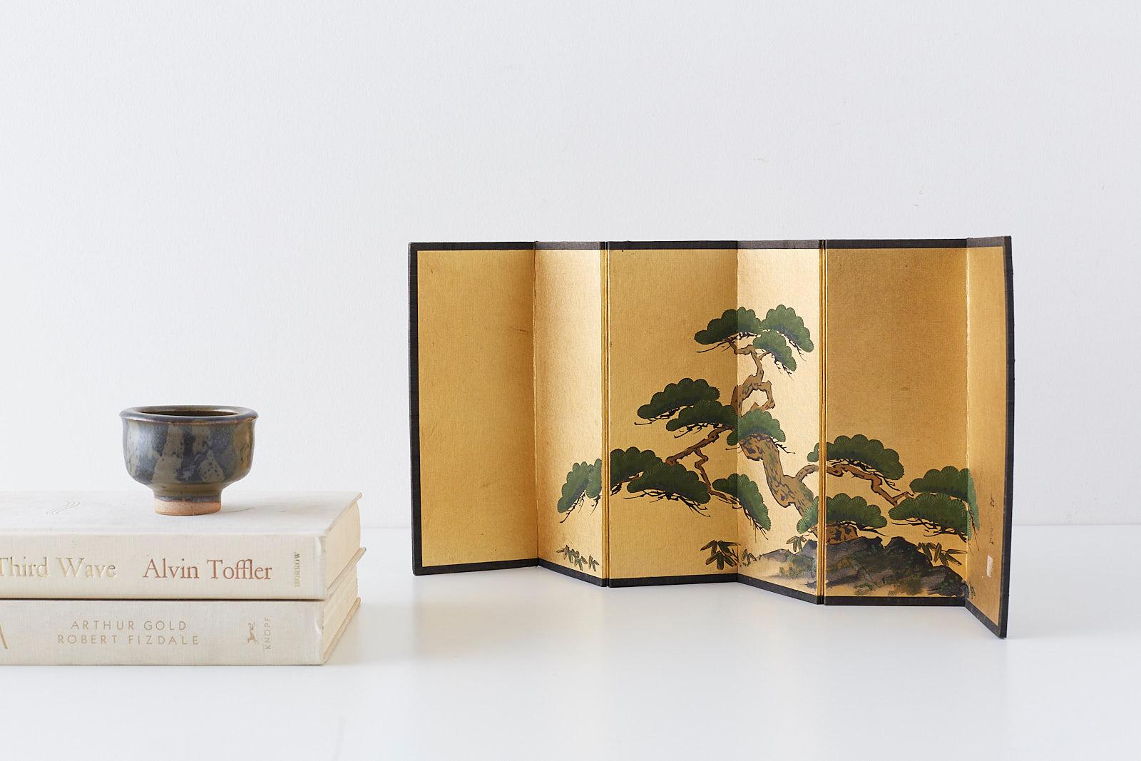 Diminutive Japanese six-panel screen in a miniature table size. Depicts an ancient pine with bamboo. Ink and color pigments on gilt metallic paper. Signed Shoku/Shokyo and one seal stamp. Printed paper verso of a scrolling vine and flower design