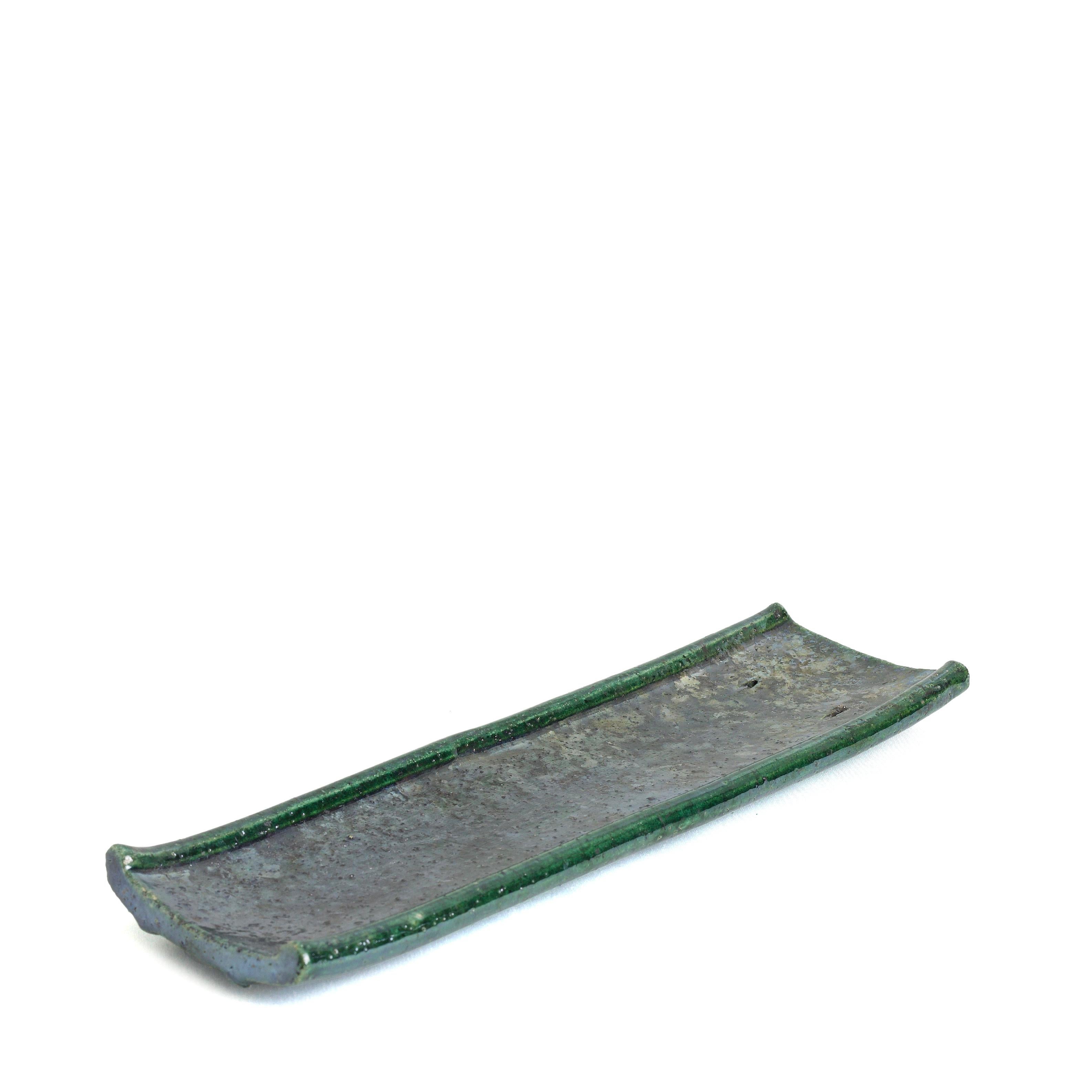 An extraordinary addition to a contemporary decor for a stunning visual allure, this incense holder features a raw, porous shape deftly handcrafted and fire with the Raku Japanese technique. This piece features green copper reflections and a wrought