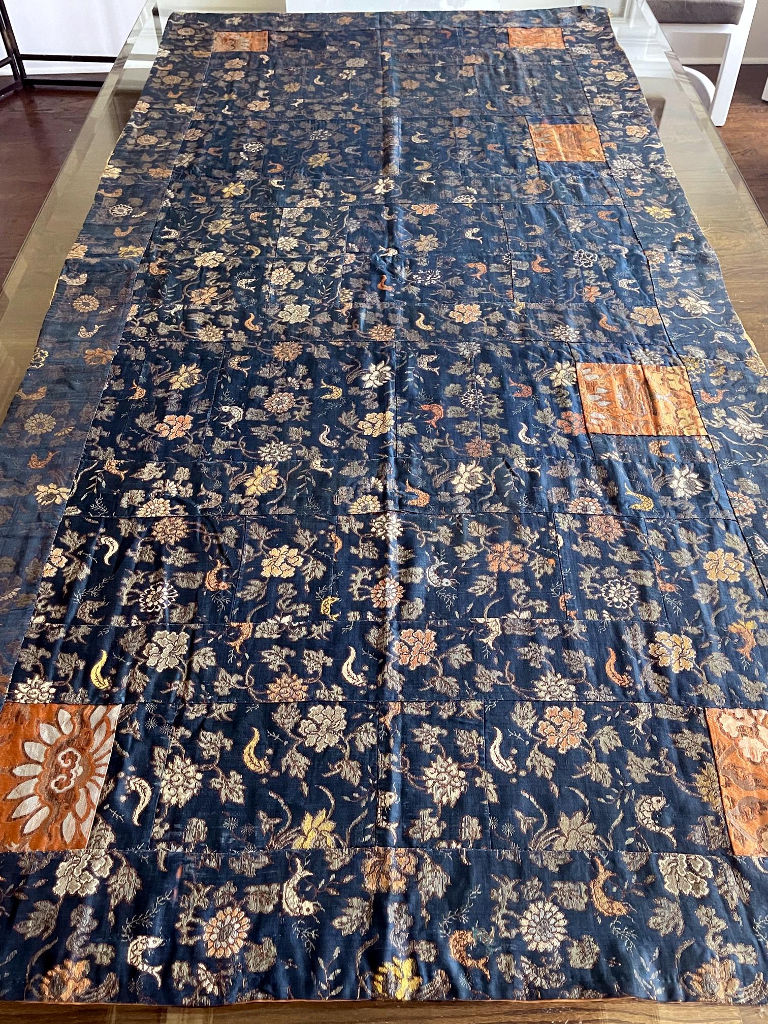 A Japanese Kesa (Monk's Vestment) made from thirteen columns of patchworks of blue brocades with sumptuous woven pattern in colored and gold threads. The elaborate motifs feature repetitive pattern of blooming peonies and schools of carp among