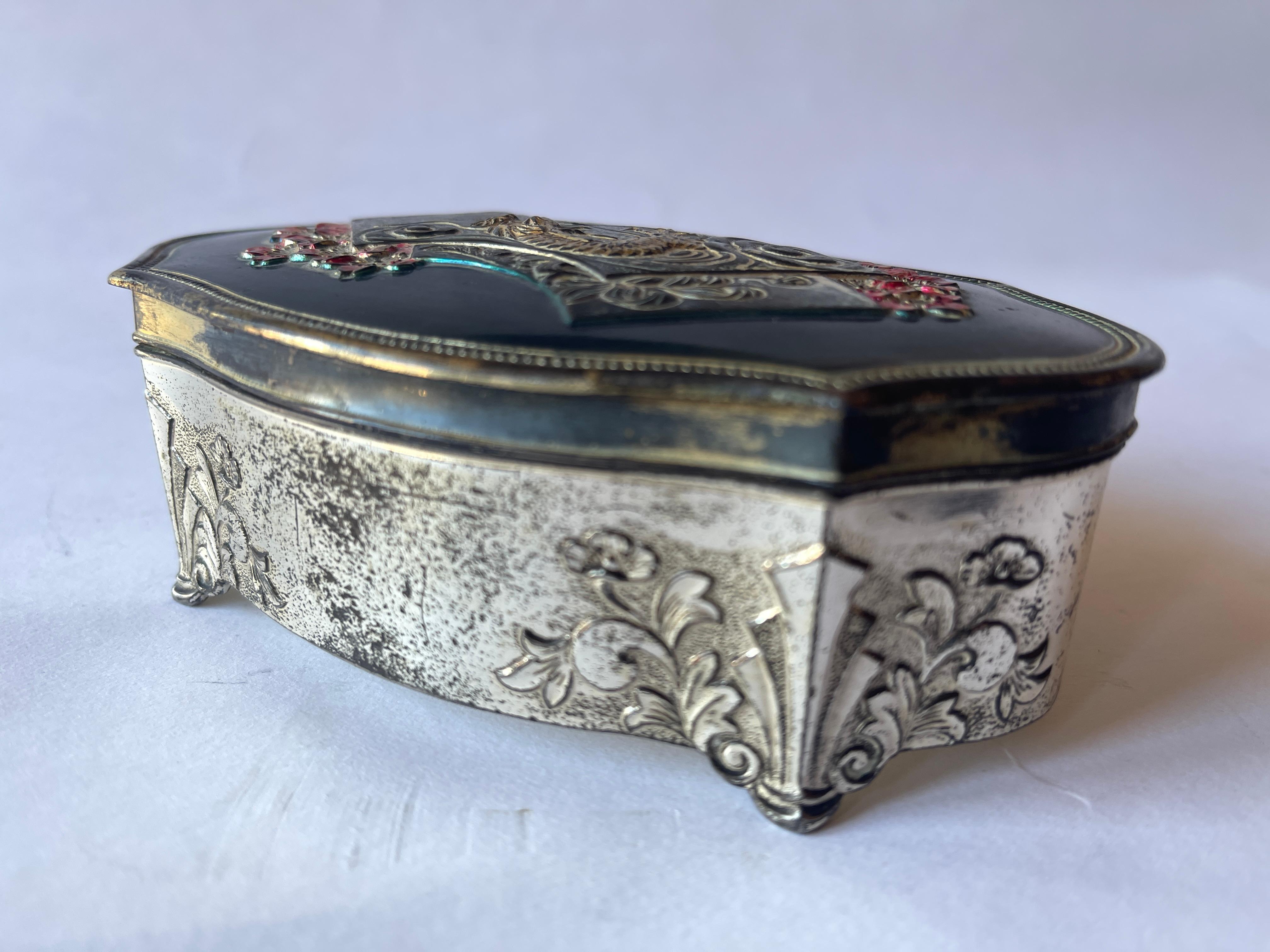 Boîte à bijoux japonaise en métal argenté dont le dessus émaillé représente le mont Fuji, entouré d'un dragon et de fleurs. Le couvercle à charnière s'ouvre sur l'intérieur en soie rose fuchsia. 
