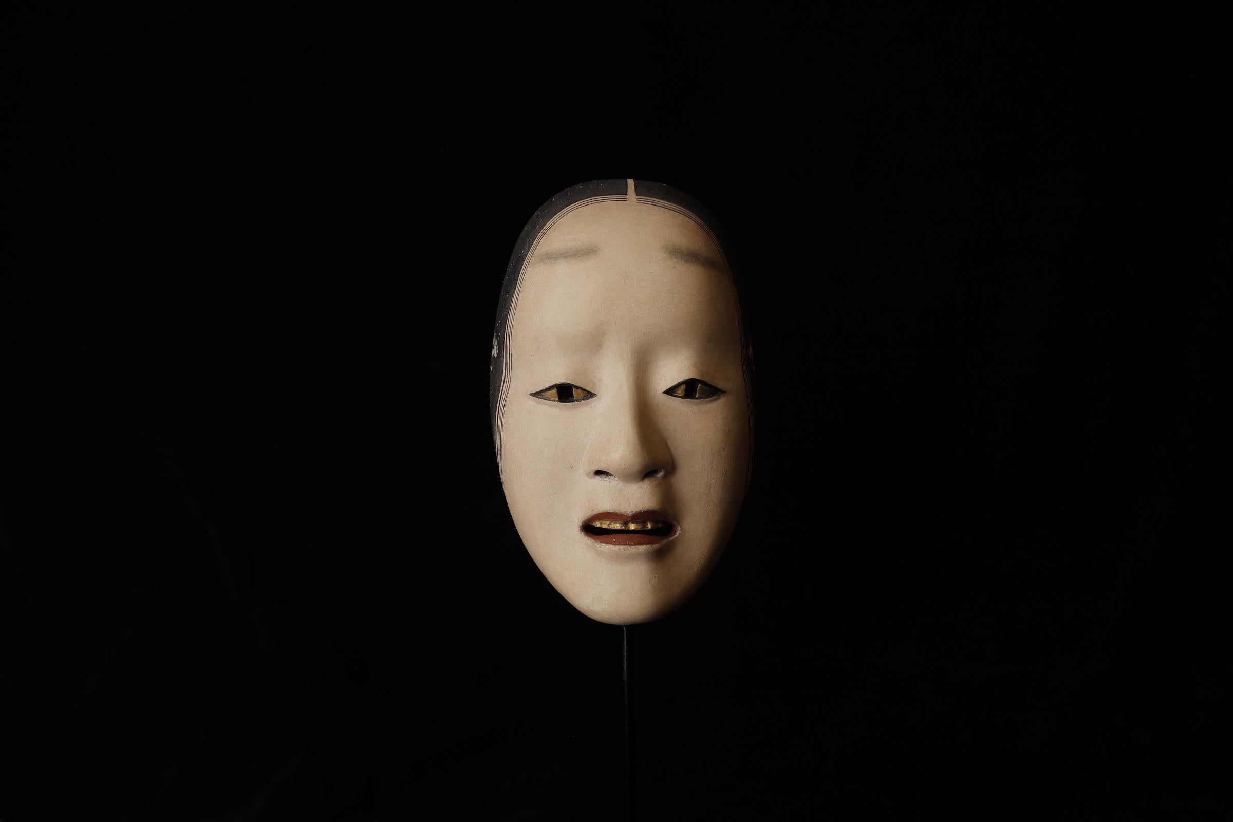 A Noh mask used to portray a female character who is possessed by a spirit or consumed by extreme emotions, such as jealousy or madness. The mask is distinctive for its gilded, metallic eyes and intense, contorted expression, which convey a
