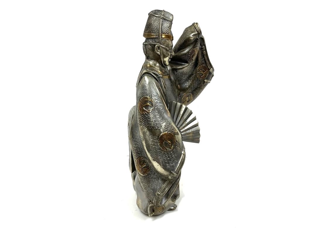 La figurine en métal mixte représente un personnage du théâtre nô,  une forme d'art traditionnel japonais ou théâtre Kabuki. Le personnage est représenté dans une tenue de théâtre traditionnelle décorée de médaillons de grues en pierre dorée et