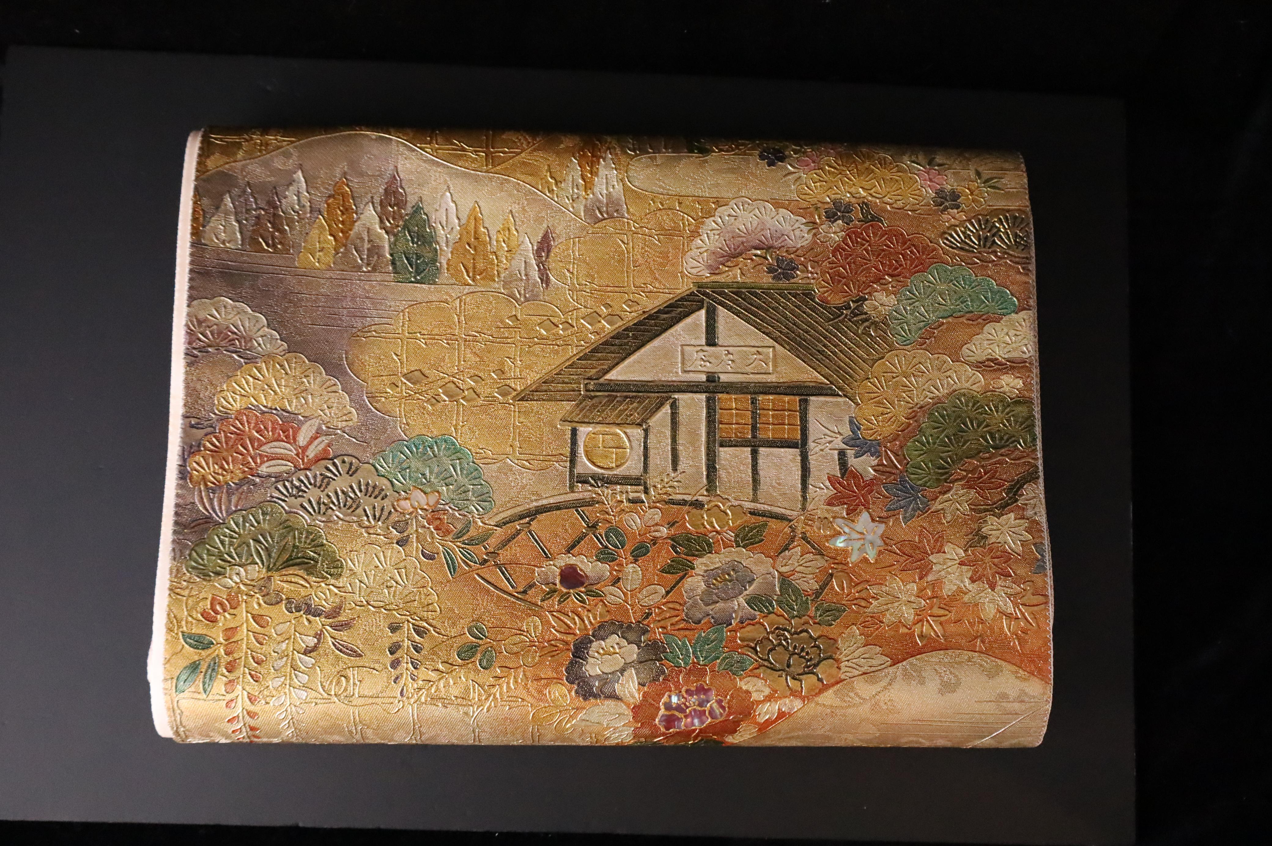 A stunning Japanese obi textile from the Shōwa period, masterfully woven from silk with exquisite raden (mother-of-pearl inlay) detailing. This formal maru obi features a rich and intricate design of a traditional pavilion set within a stylized