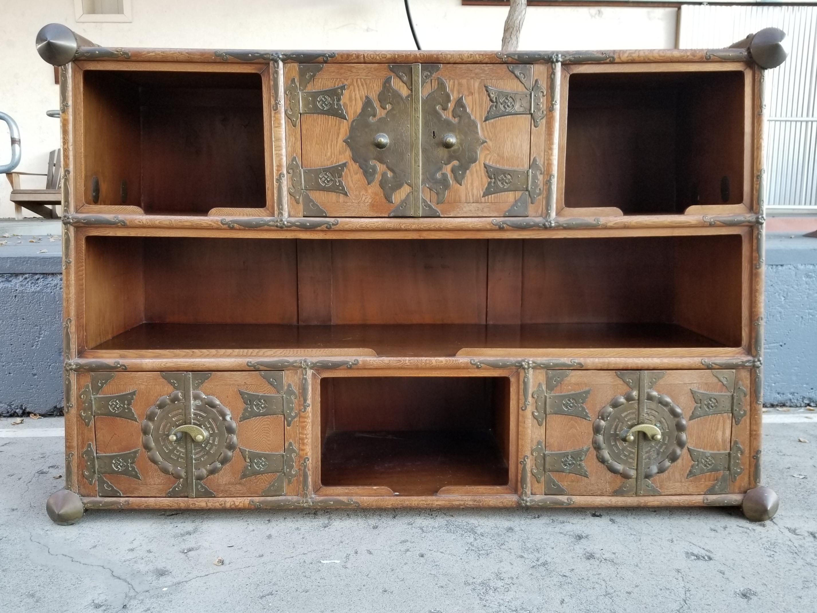 Unusual early 20th century Tansu with elaborate brass work and canted sides. Three pairs of cabinet doors exposing interior drawers and storage accompanied by open shelving. Dramatic upper and lower brass corner decoration. Large-scale brass handles