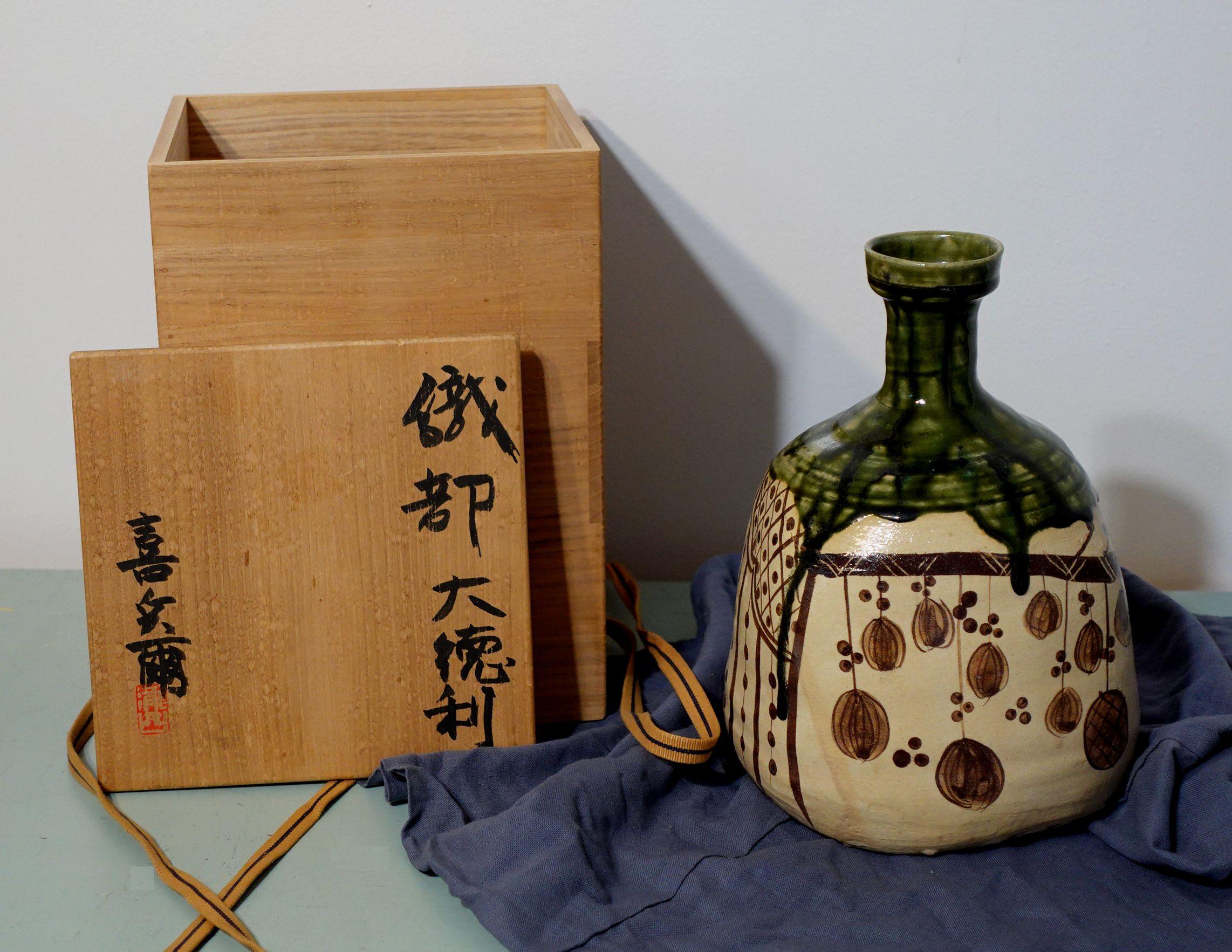 Japanese Oribe Stoneware/Sake vase w/ original box and cloth
This is a large Sake Bottle with a wide mouth vase and green glaze drip decorated with botanical designs including the original wood box and cloth

Dimensions
Vase 10 1/4