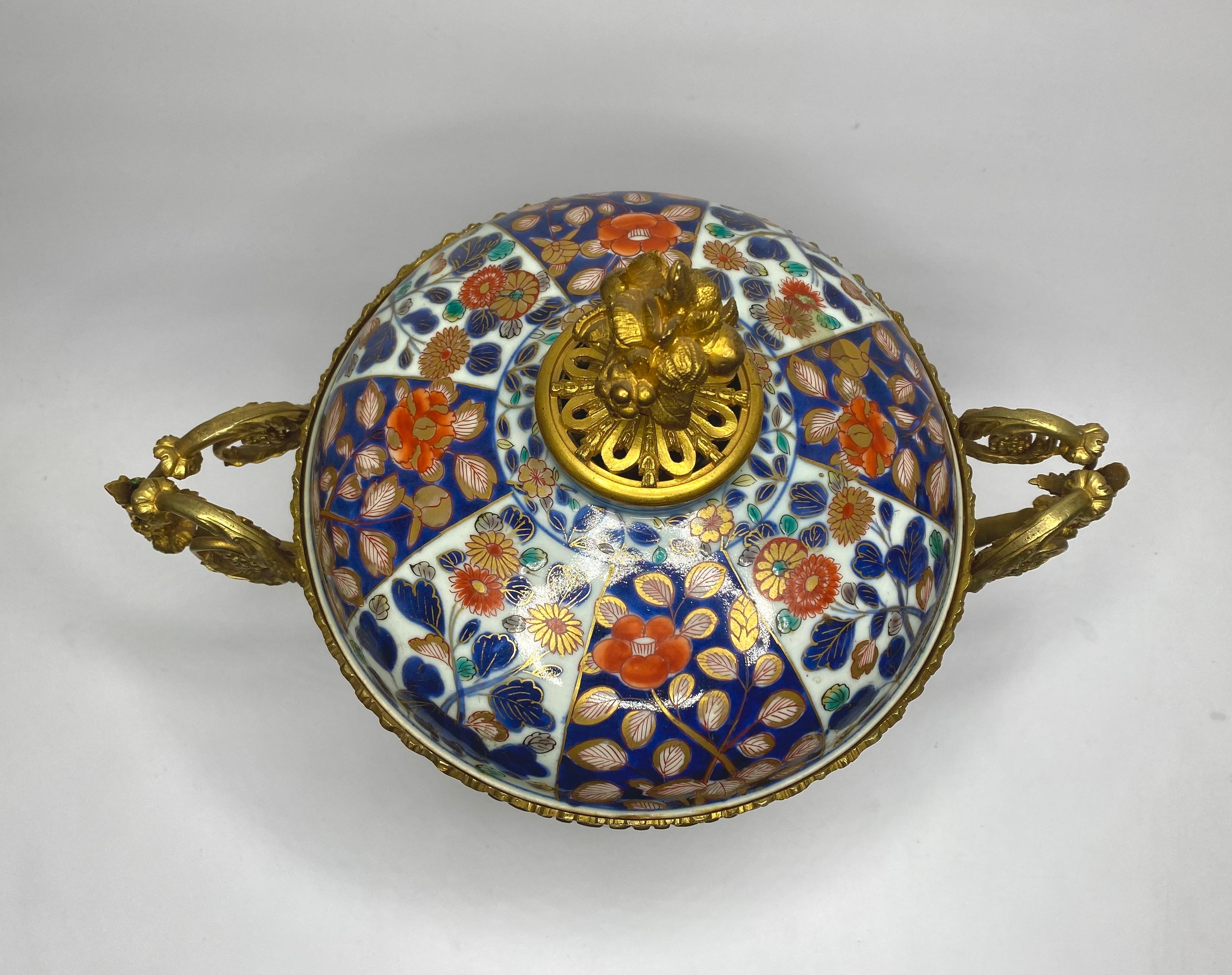 A large Japanese Imari bowl and cover, c. 1700, Arita, Edo Period, with 19th Century French ormolu mounts. The deep sided bowl, hand painted with alternating panels of flowering plants, in typical Imari enamels, heightened in gilt. The footrim with