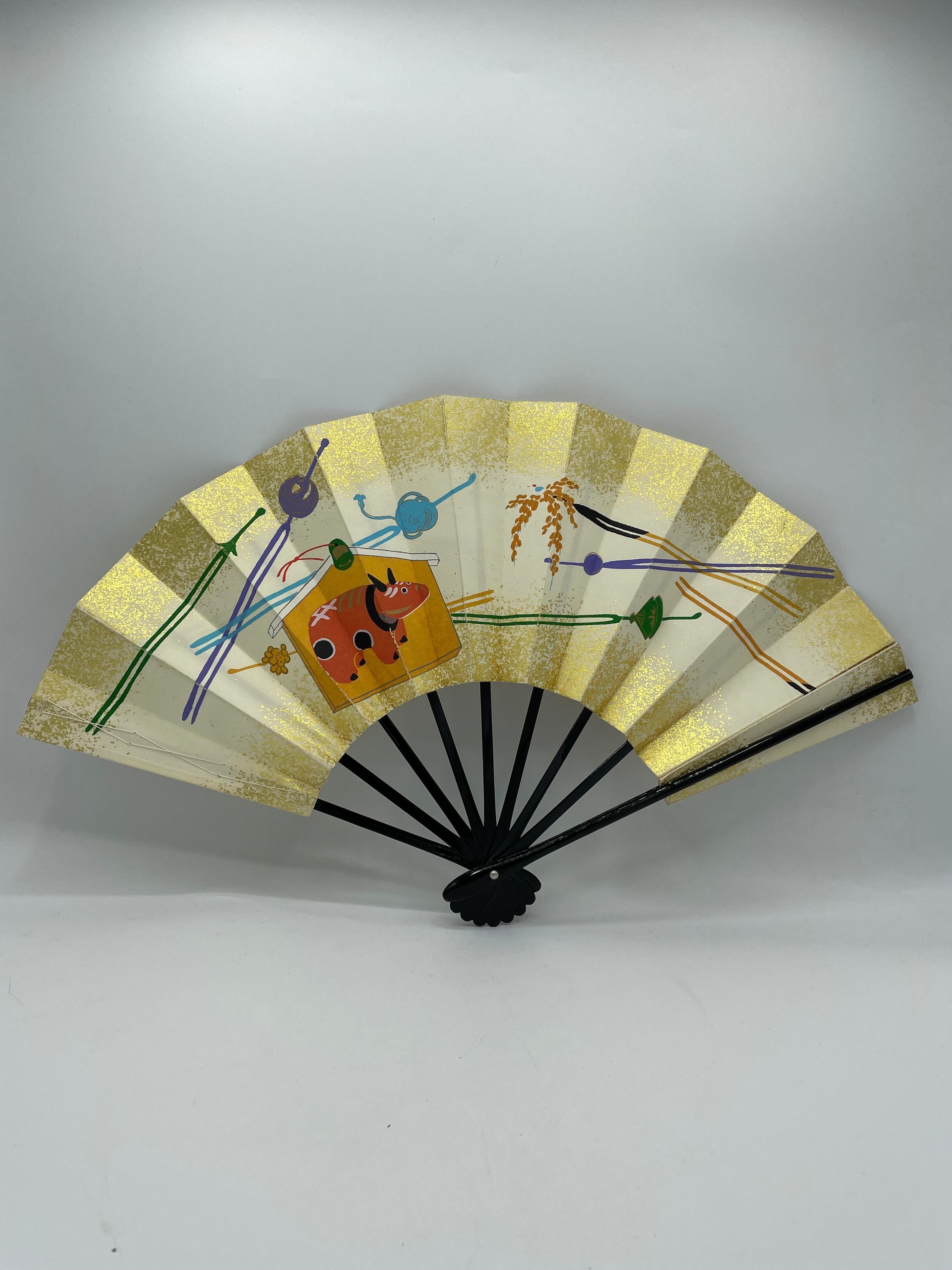 This is a fan which was made in Japan around 1980s in Showa era. 
This material is Paper and wood and there are little threads with cotton on the side. 
Both sides are same designs of Akabeko and Kanzashi.

Japanese fans are made of paper on a