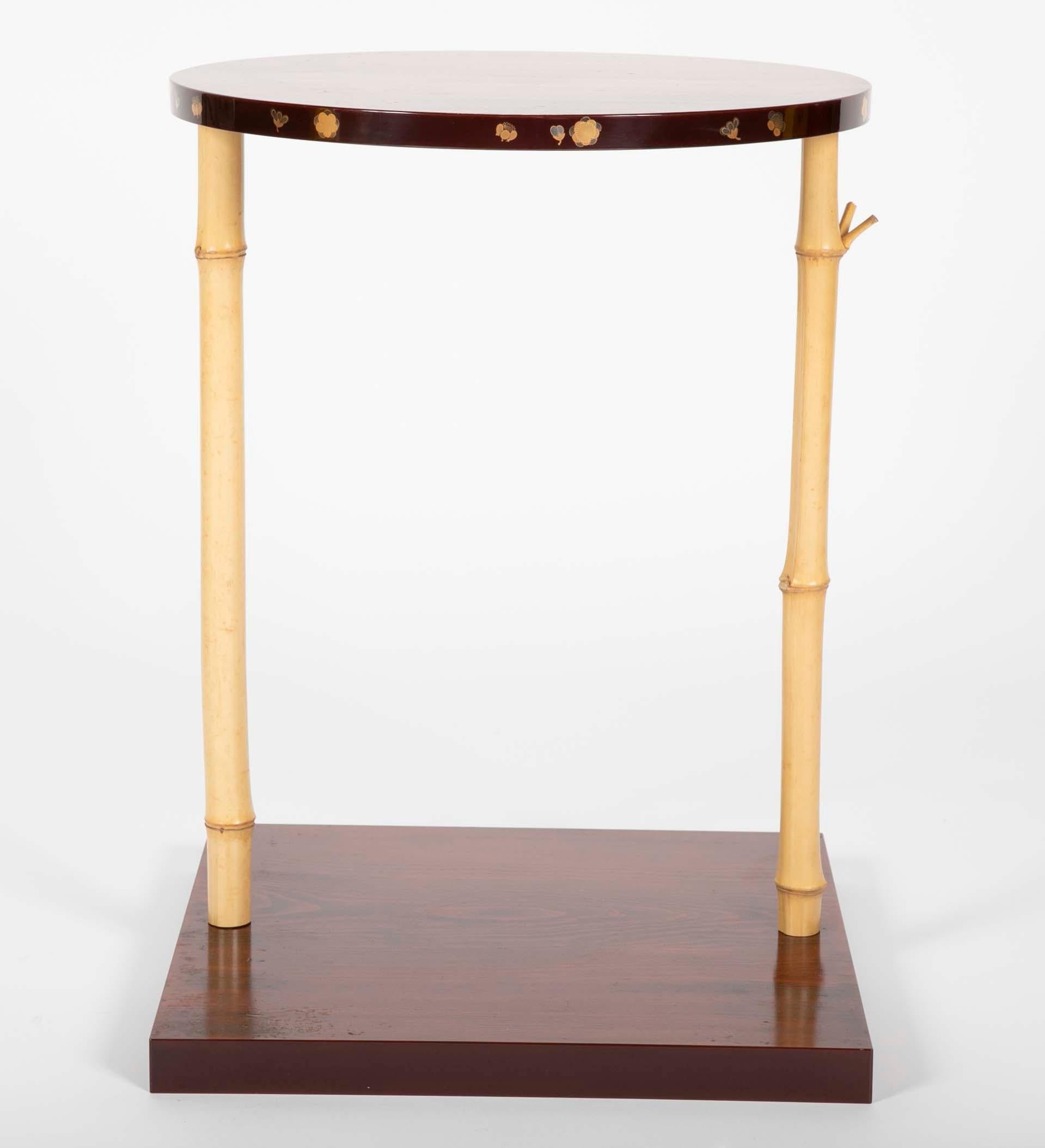 Une table d'appoint japonaise exceptionnellement minimaliste et ludique, avec un plateau circulaire en pin, reposant sur deux pieds en bambou amovibles et une base carrée en pin. Les bords des pièces supérieures et inférieures sont laqués. La base