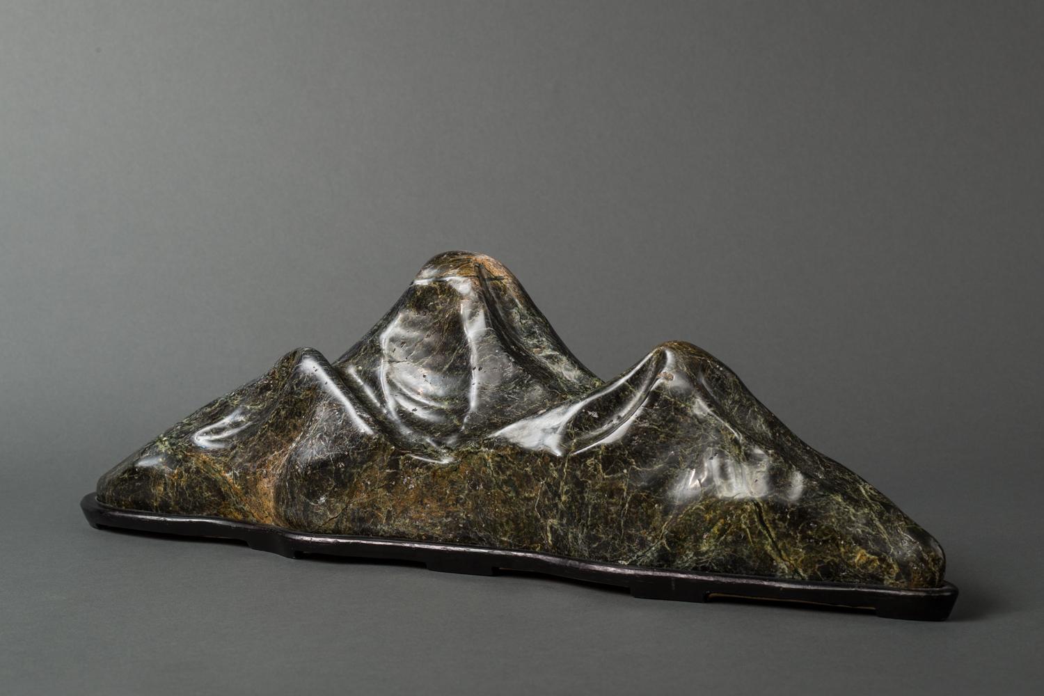 Japanese polished spirit stone in the shape of a mountain range, archaic polished stone with beautiful veined green color simulating a mountain range, set in a handmade custom hardwood base.