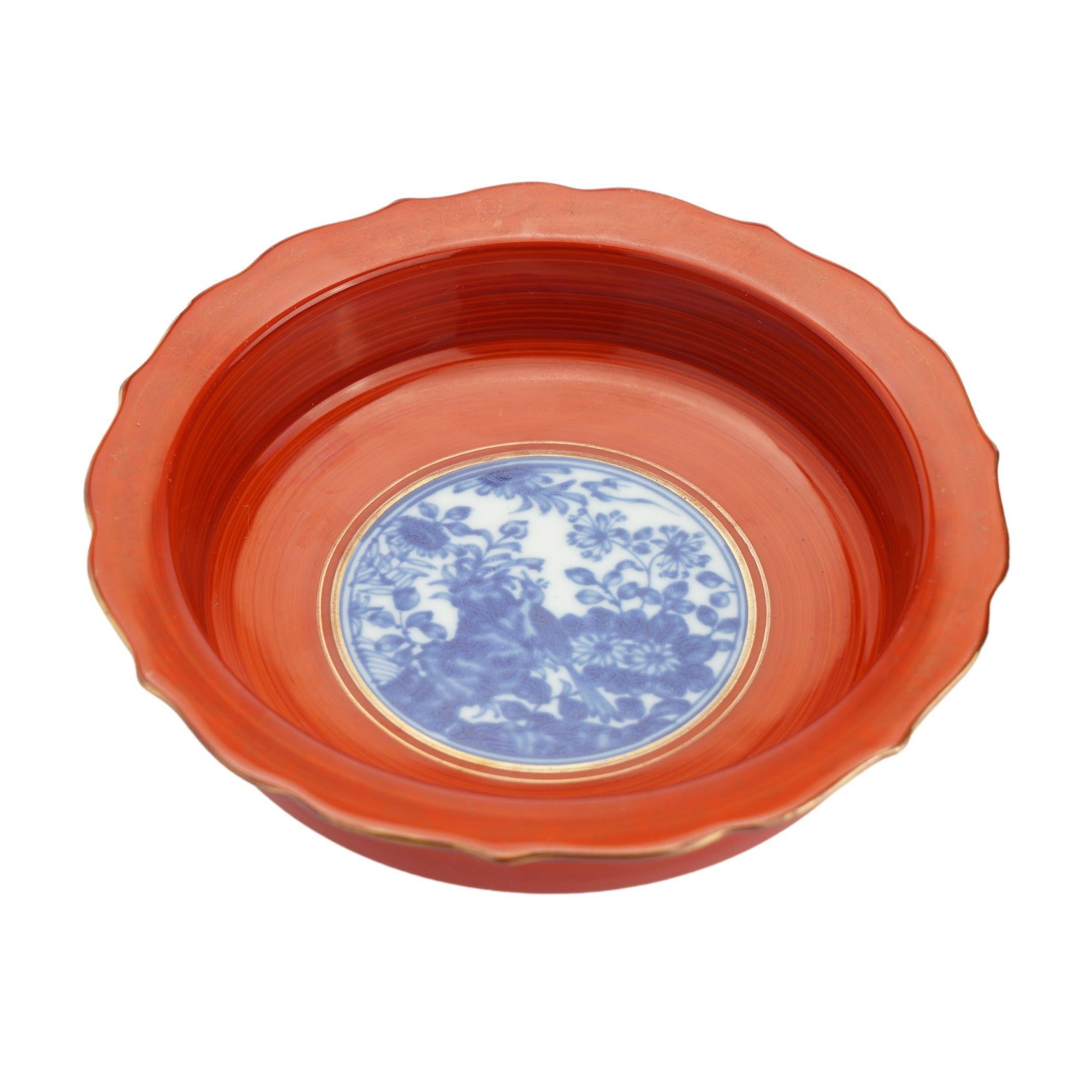 Japanese coral red enameled porcelain bottle coaster, with standing edge and flaring scolloped rim, centering on a circular idealized landscape rendered in cobalt under glaze blue. Japanese chop in cobalt under glaze blue on the underfoot. 
Japan,