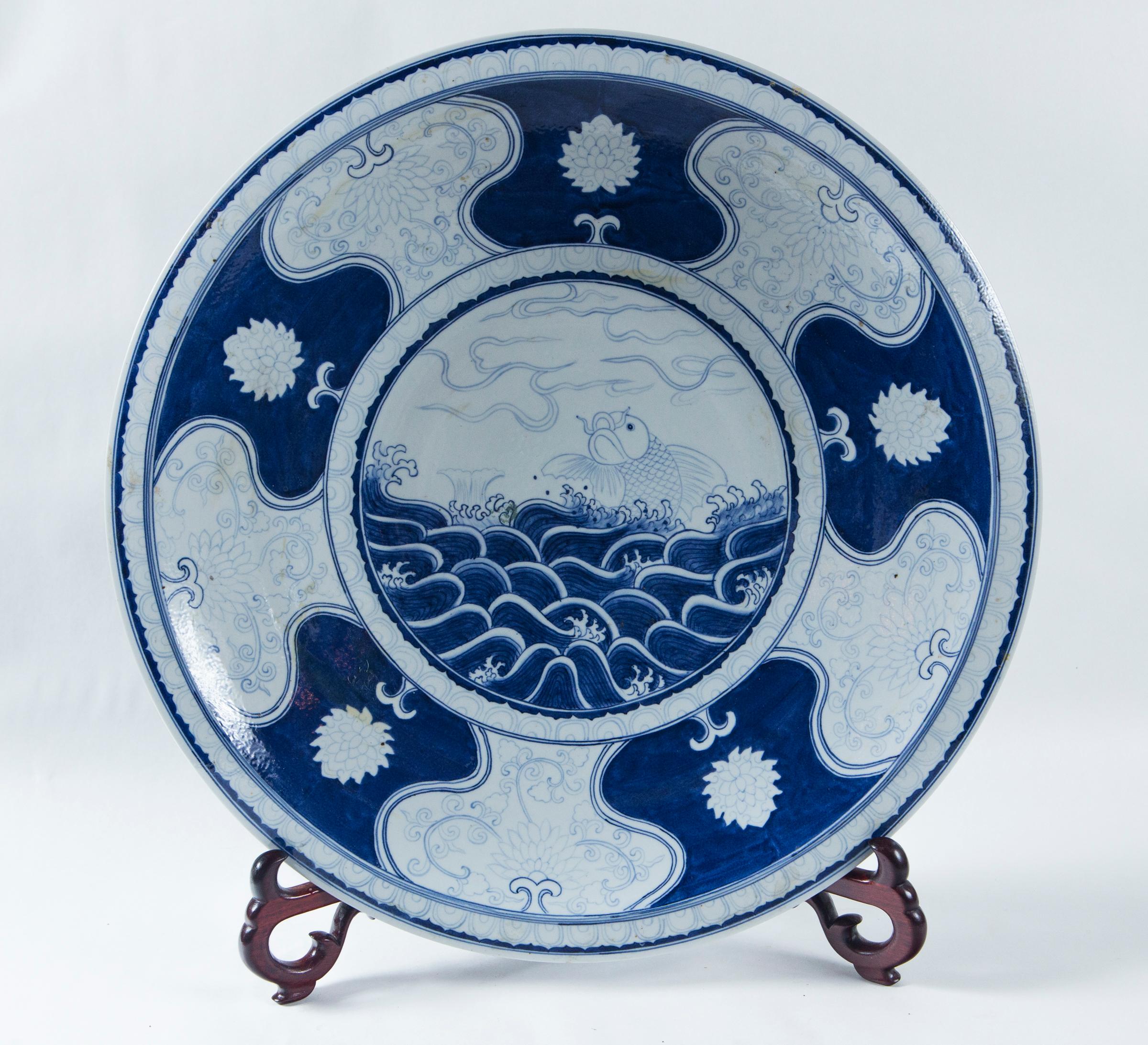 Decorated in in cobalt blue, with ocean waves and a jumping fish in the center. Surrounded by lobe shapes and flowers, possibly chrysanthemums. The outside decorated with plaques of floral and tendril design.