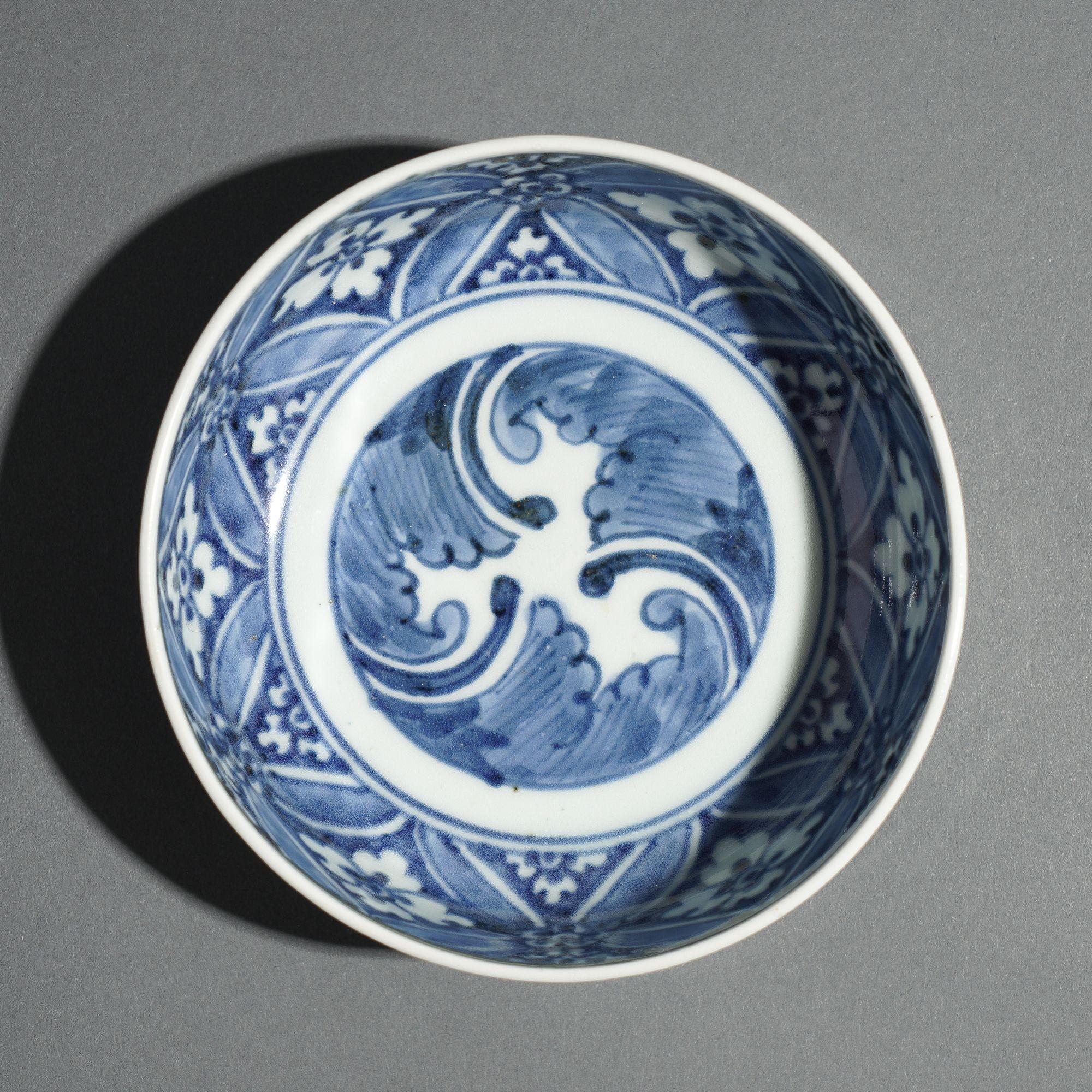 Traditional, vertical sided porcelain footed bowl with a bold diapered pattern in cobalt underglaze blue on the interior rim which centers on a swirling trefoil wave design. The exterior has a running vine around the circumference. The underfoot