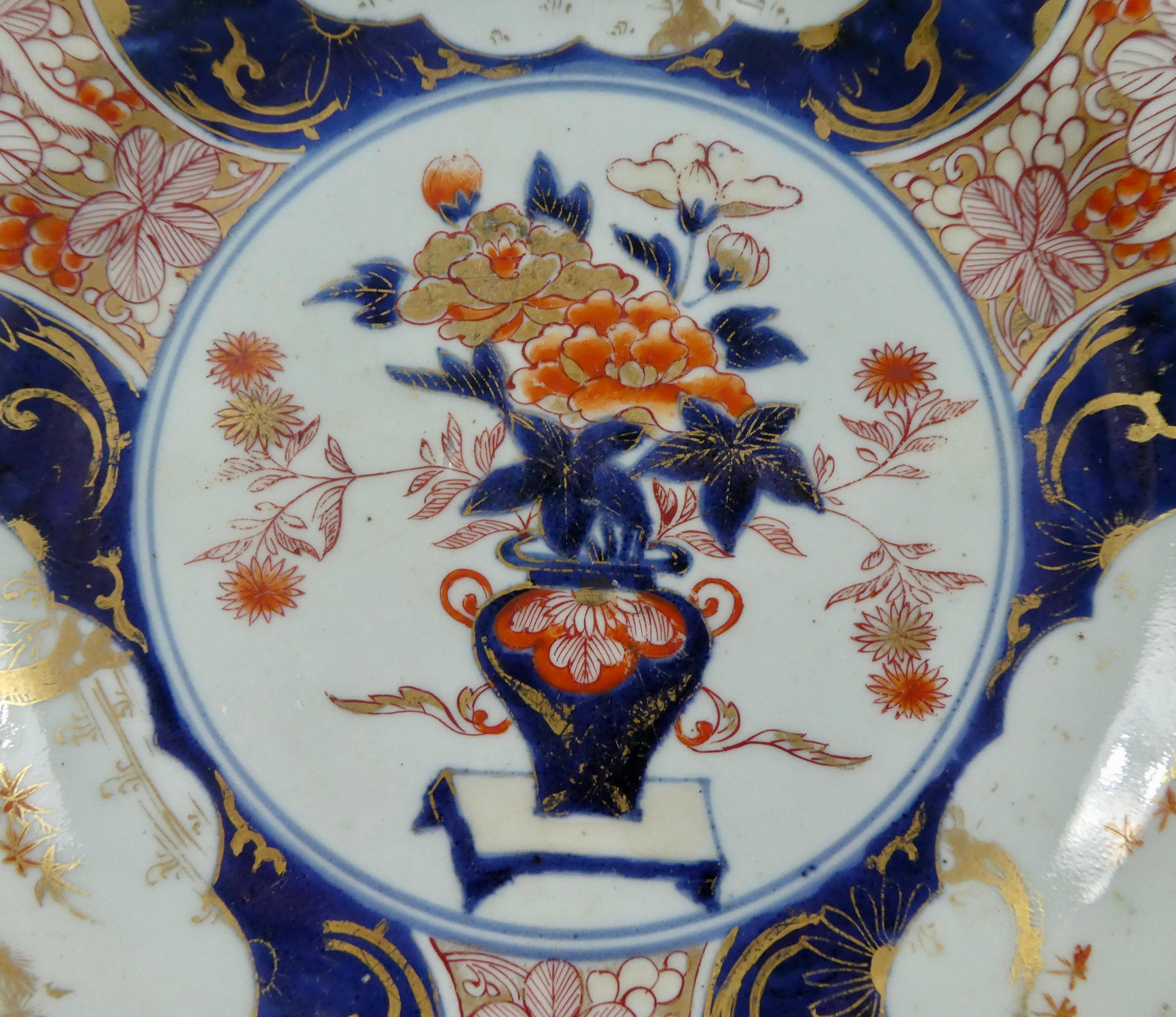 Japanisches Porzellangeschirr:: Arita:: um 1700:: Genroku-Periode. Die große Schale:: gut gemalt im Imari-Stil:: mit einem zentralen Panel einer Vase mit blühenden Pflanzen:: auf einem Tisch. Die breite Bordüre ist im typischen Stil mit Tafeln mit