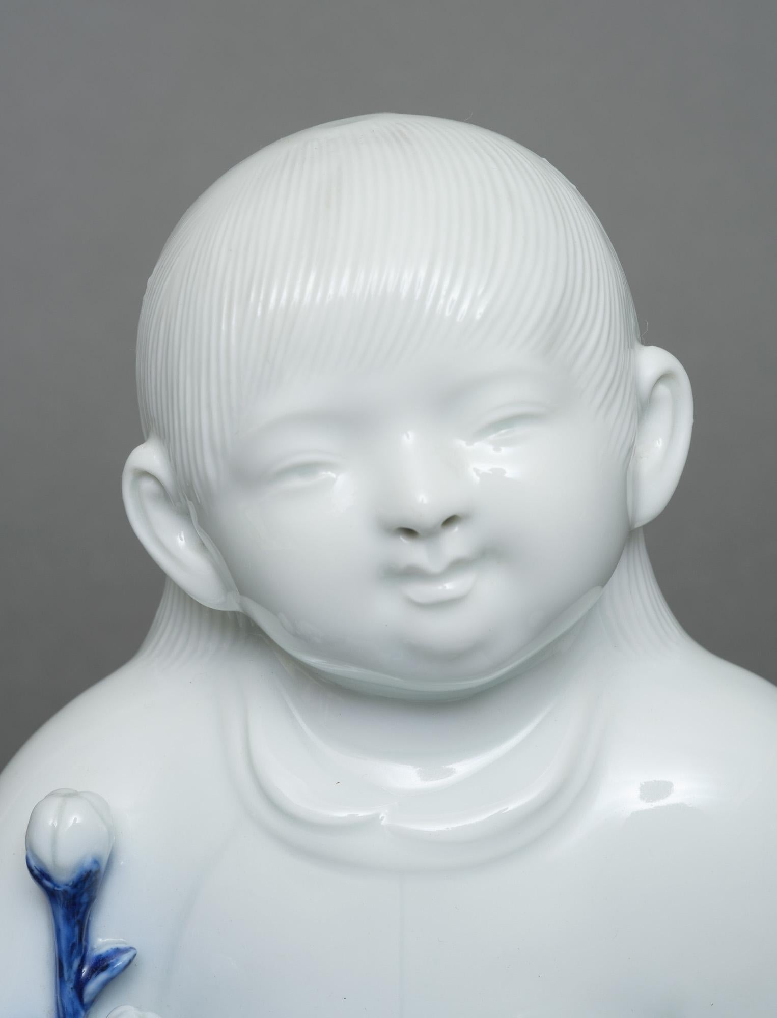 Exquisite white glazed porcelain figure (okimono) of a sitting child holding a spray of chrysanthemum flowers with cobalt blue glazed leaves in its hand, by Sakaida Kakiemon XII (1878–1963).

The milk white glaze is called nigoshide a type of