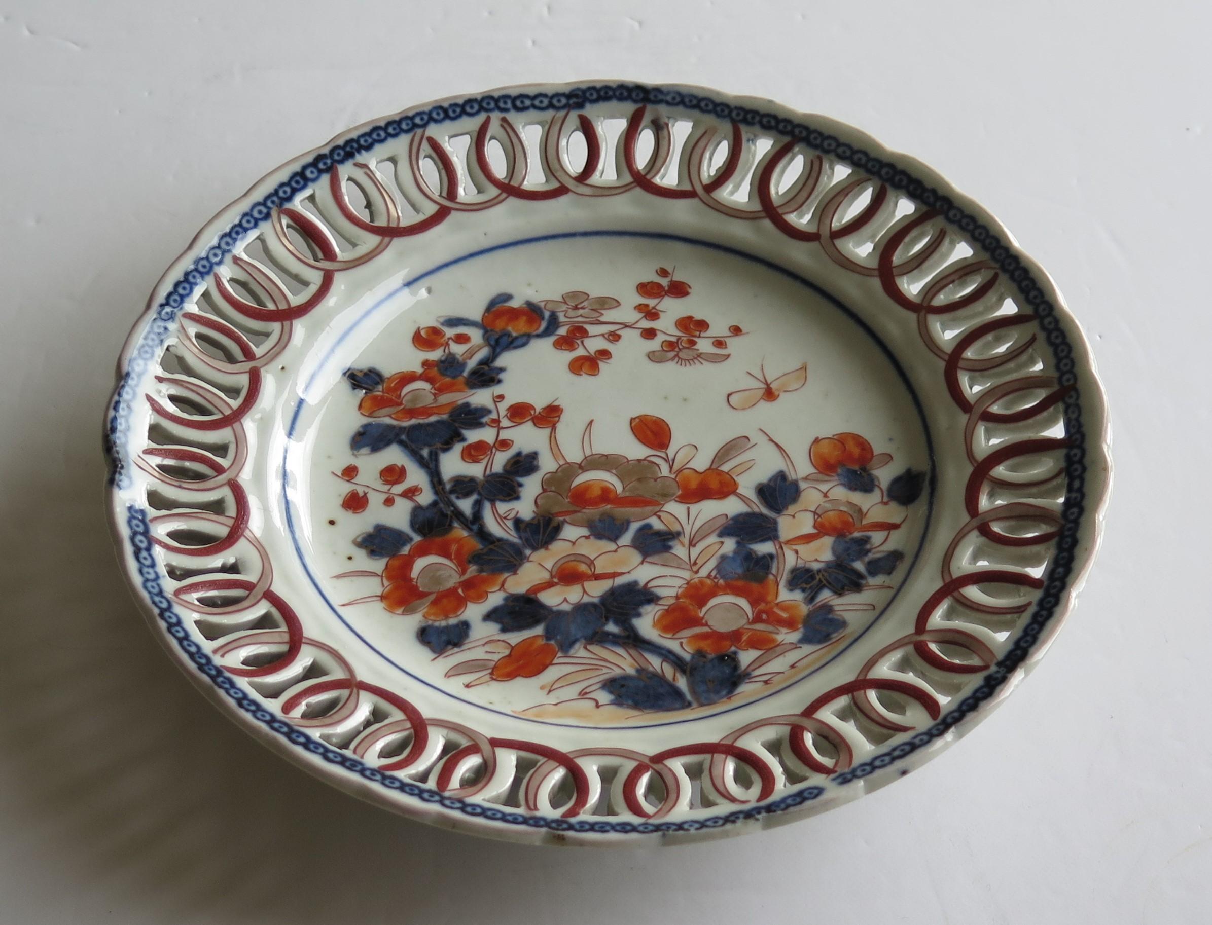 This is a good quality Japanese porcelain plate or shallow dish, of reticulated form with an interlinking open chain formed around its outer rim, which we date to circa 1800. 

The plate is decorated in the Imari style with varying shades of