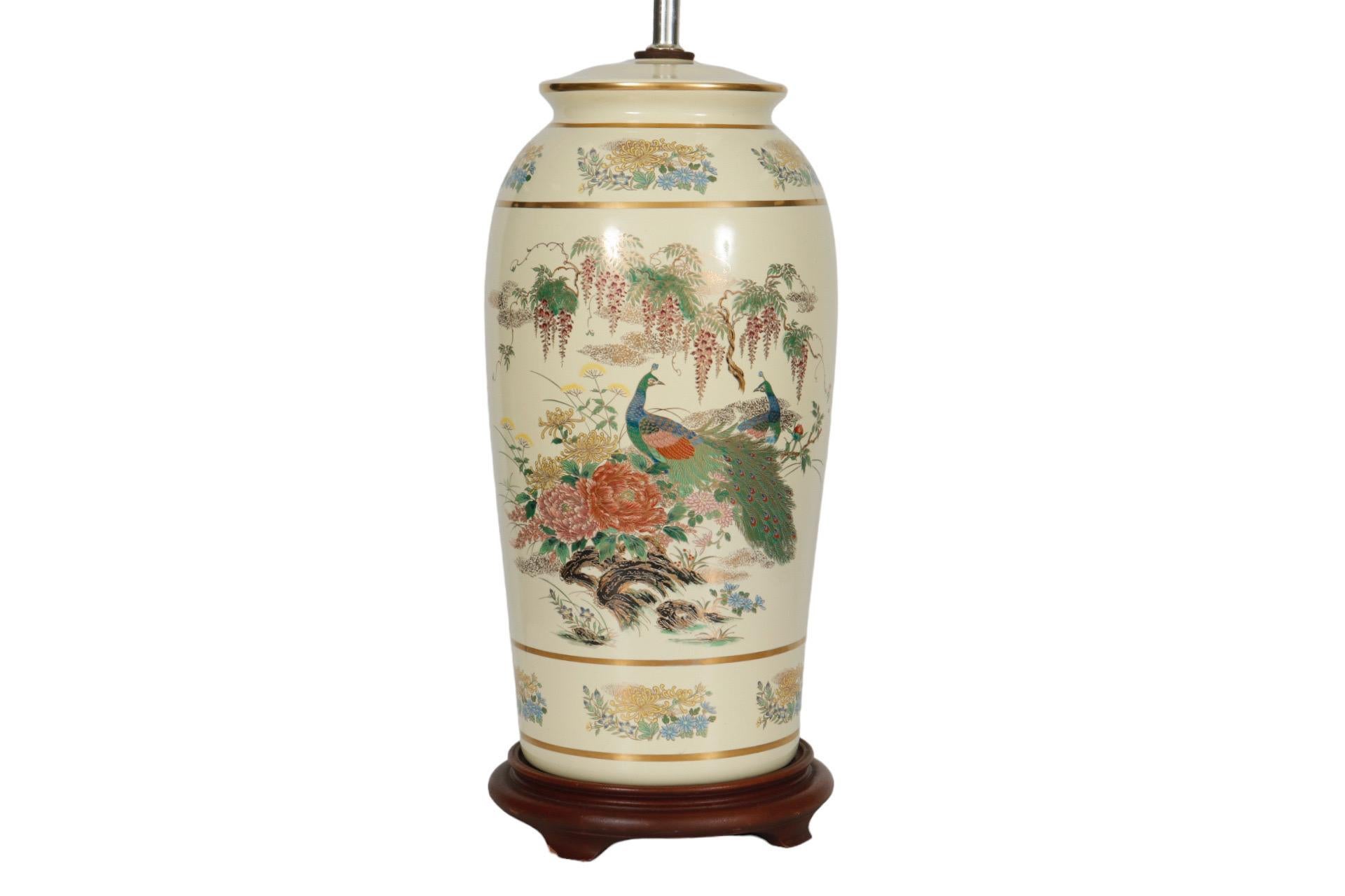 A Japanese style porcelain table lamp mounted on a brown beveled base. Richly painted with colorful peacocks and blossoms overlaid with gold. Topped with a brass finial pierced with a geometric motif. Wired and in working condition. Measures 22.25