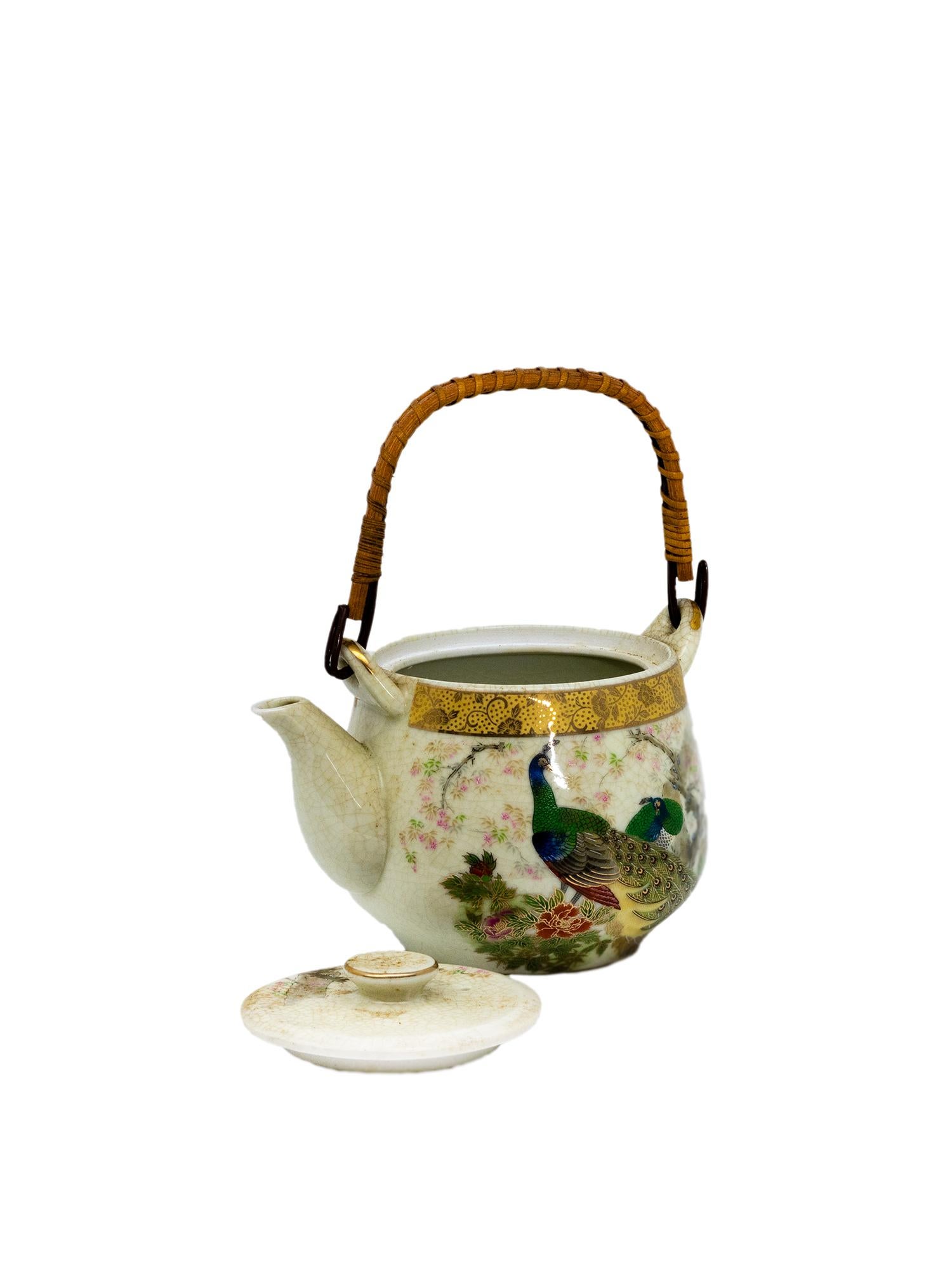 Delicadamente elaborada en Japón durante el siglo XX, esta encantadora tetera de porcelana presenta una pareja de regios pavos reales en vibrantes tonos esmeralda, azul y dorado, que se yerguen graciosamente entre rosados cerezos en flor. Sobre un