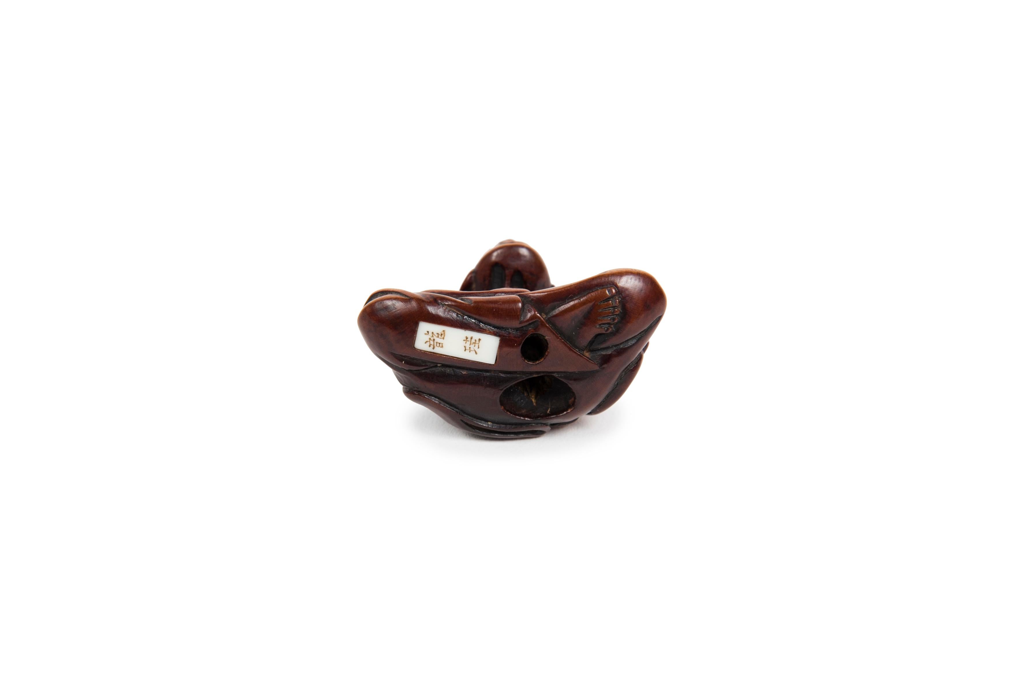 Boxwood netsuke of a seated professional sneezer depicted as an old man with his right hand raised, holding an stick to tickle himself. His head is slightly raised, his eyes practically closed and his mouth wide open, signs that he is about to