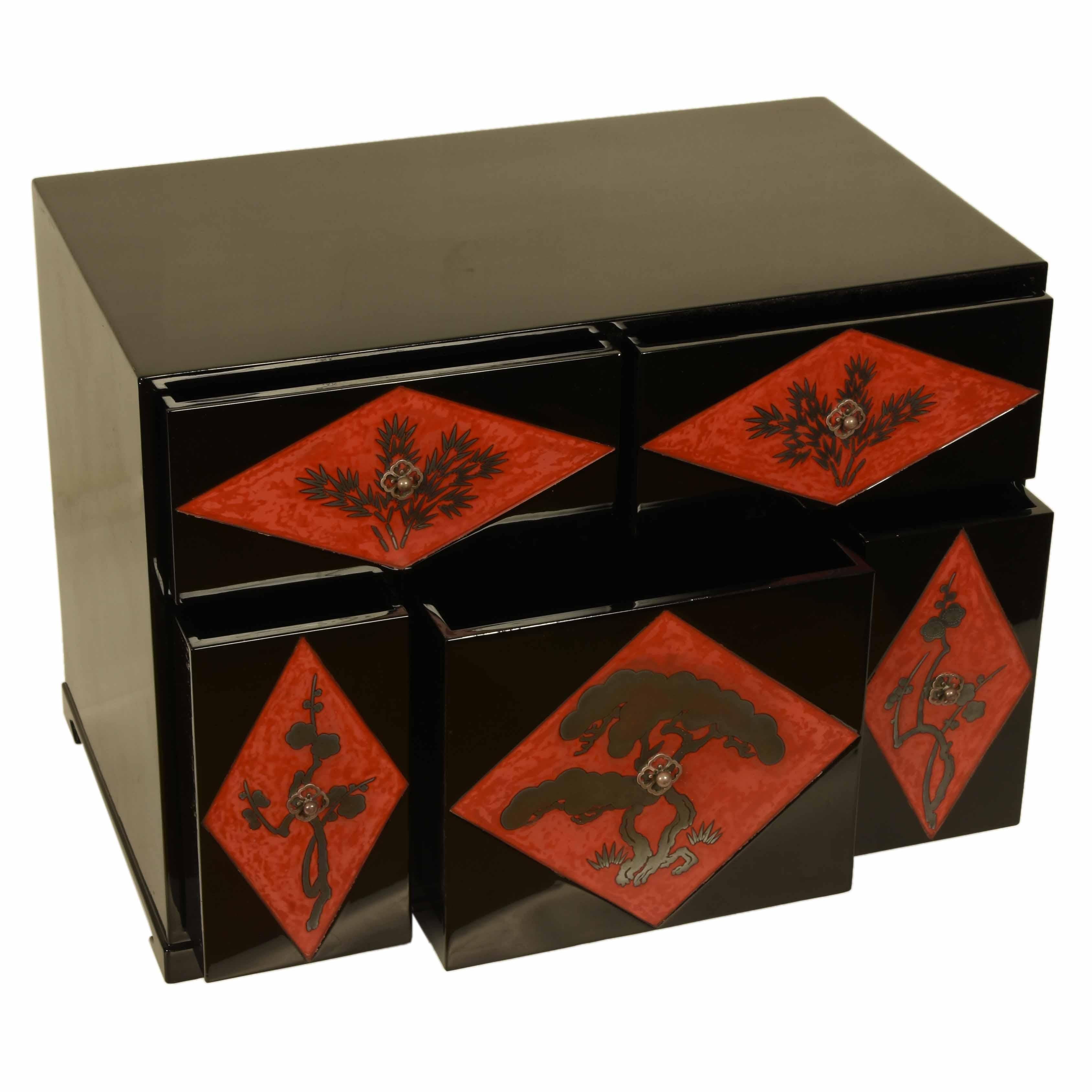Eine antike japanische Kommode mit fünf Schubladen, schwarz lackiert. Jede Schubladenfront ist mit einem silbernen Kiefer- und Blütendekor versehen, das von einem grafischen, rot lackierten Rautenhintergrund umrahmt wird. Die Beschläge sind ebenso