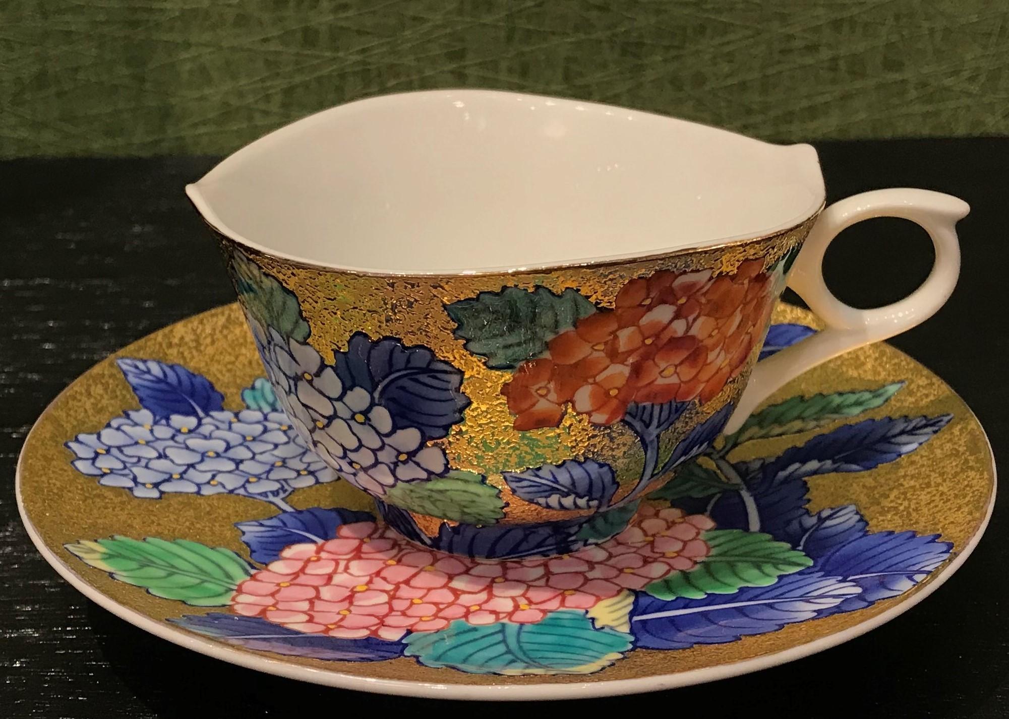 Exquisite contemporary gilded fine porcelain cup and saucer, intricately hand painted in vivid blue, red and pink on an attractive gilded body, featuring stunning hydrangeas in full bloom. This cup and saucer is from a signature series by a highly