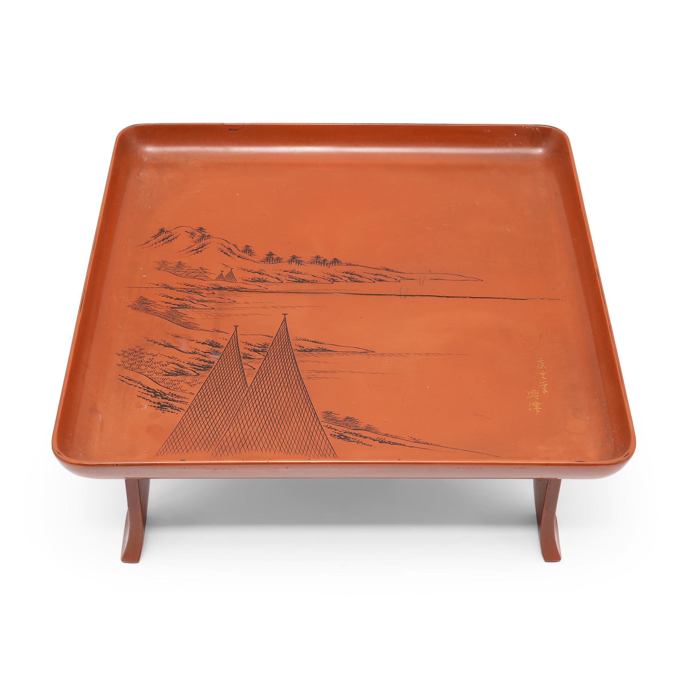 This Japanese serving tray exemplifies the refined style of Meiji-era lacquerware. Elevated by a splayed footed base, the tray has a shallow, square top with raised sides and rounded corners. The tray top is decorated with a serene mountain