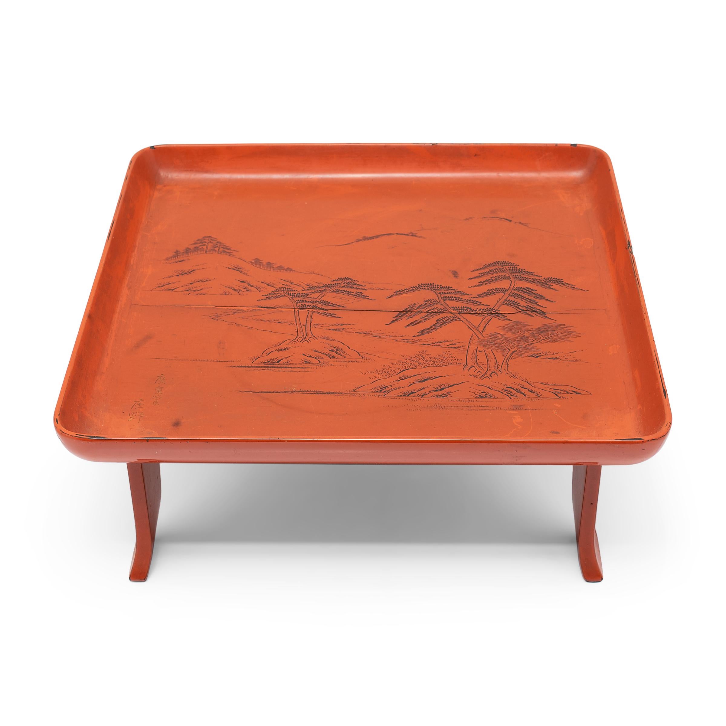 This Japanese serving tray exemplifies the refined style of Meiji-era lacquerware. Elevated by a splayed footed base, the tray has a shallow, square top with raised sides and rounded corners. The tray top is decorated with a serene sansui landscape,