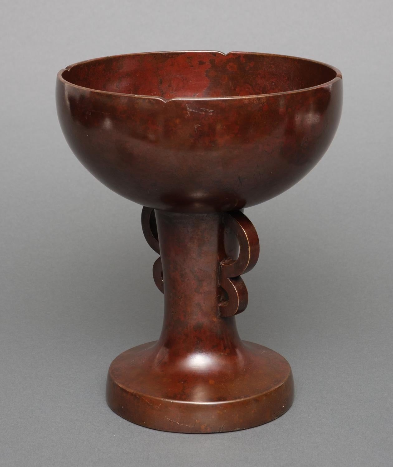 Exceptionally shaped bronze vase with a striking ‘coarse’-textured red mottled patina. The bowl subtly shaped like a flower, its slightly concave body flanked by ‘butterfly wing’-shaped ears, transcending in a circular foot with a broad