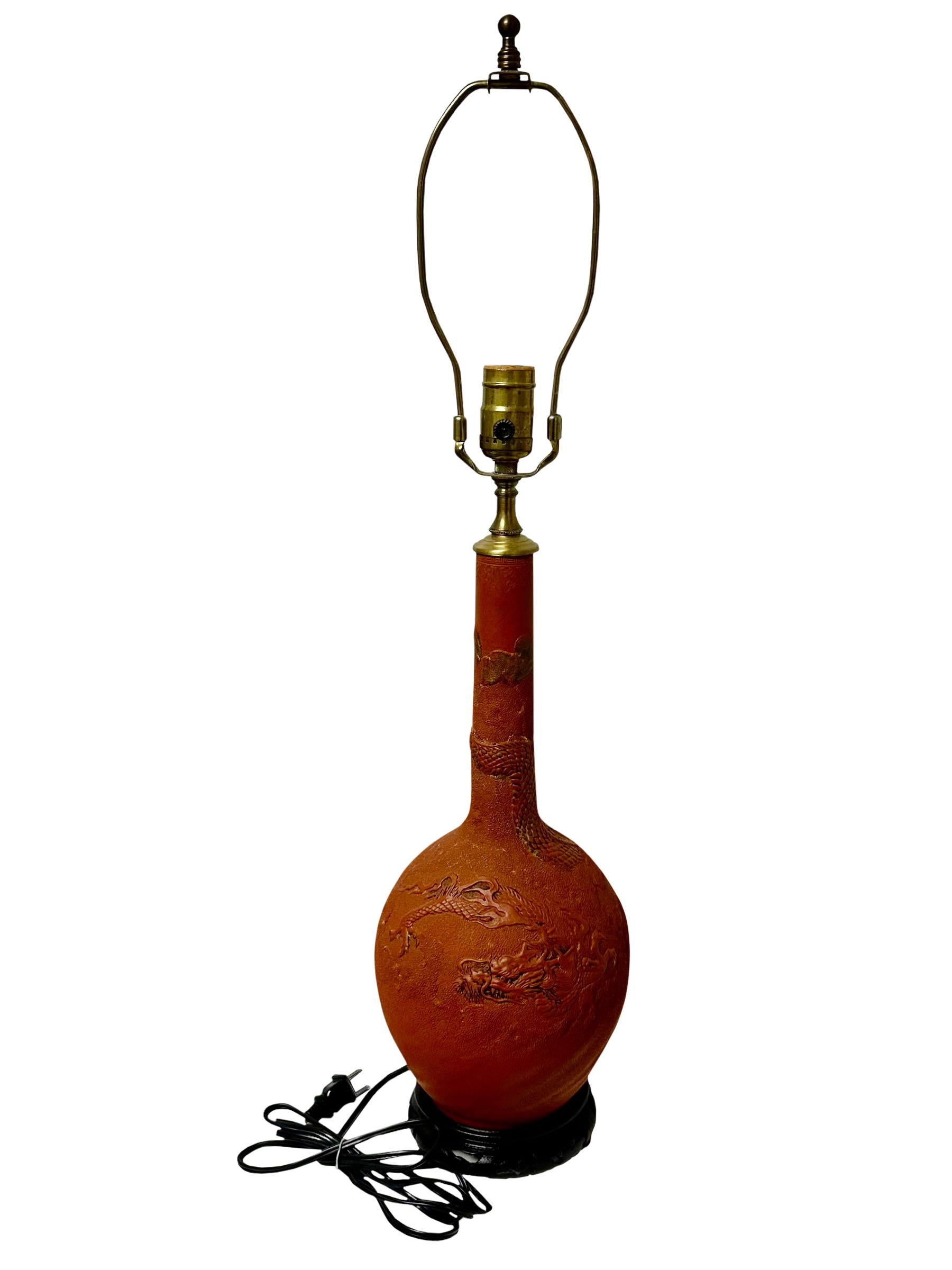 Lampe japonaise ancienne en faïence rouge décorée de dragons. Socle chinois en bois brun foncé. La lampe date du début du siècle et a été transformée en lampe probablement dans les années 1980. Elle est dotée d'un petit embout en laiton. Circa 1915,
