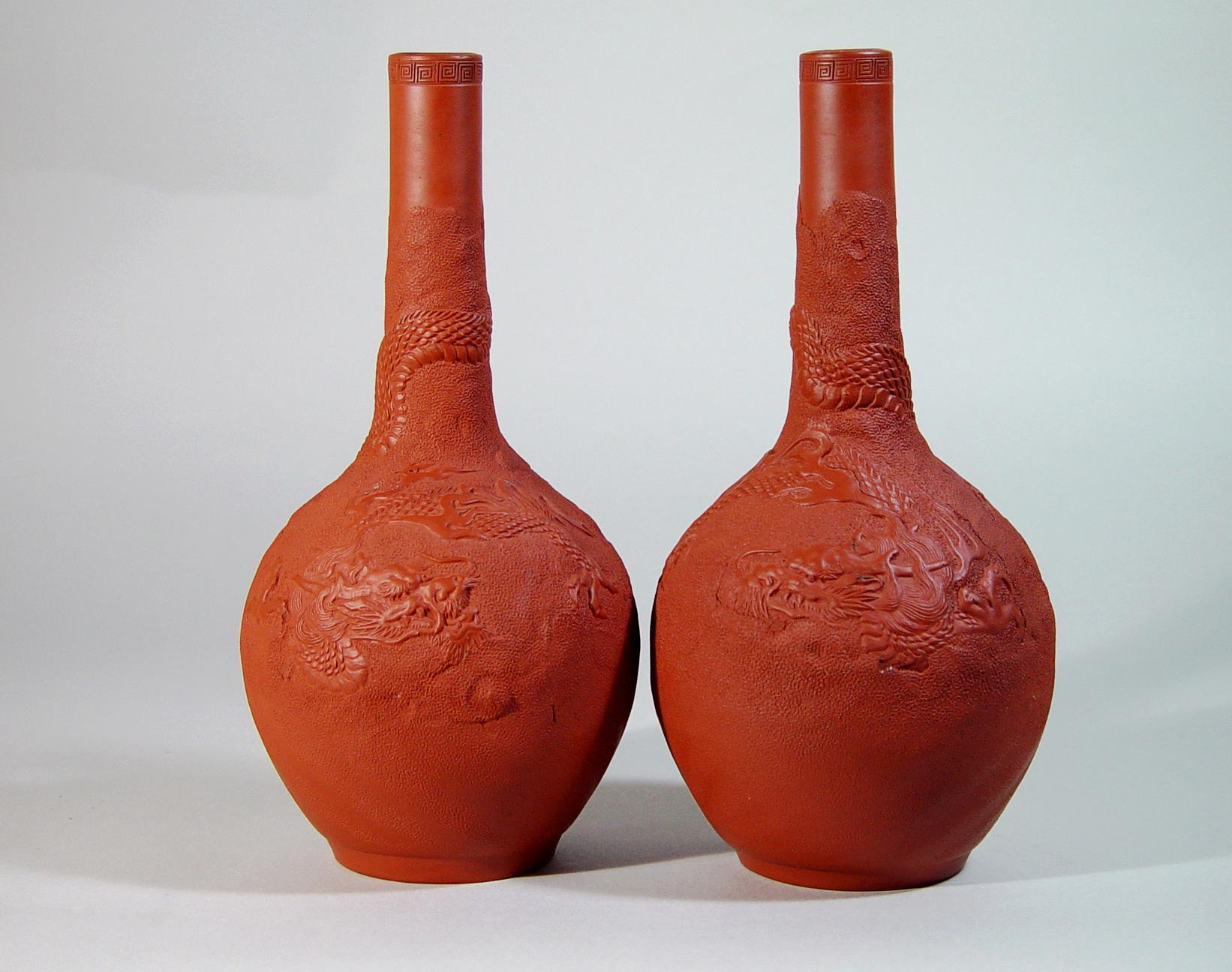 The bottle-form redware vases are decorated with a moulded design of a three-clawed scaled dragon, its tail and body entwining the vase against a pricked raised ground. The rim with a band of Greek key design.

Marks: square mark: Dai Nihon