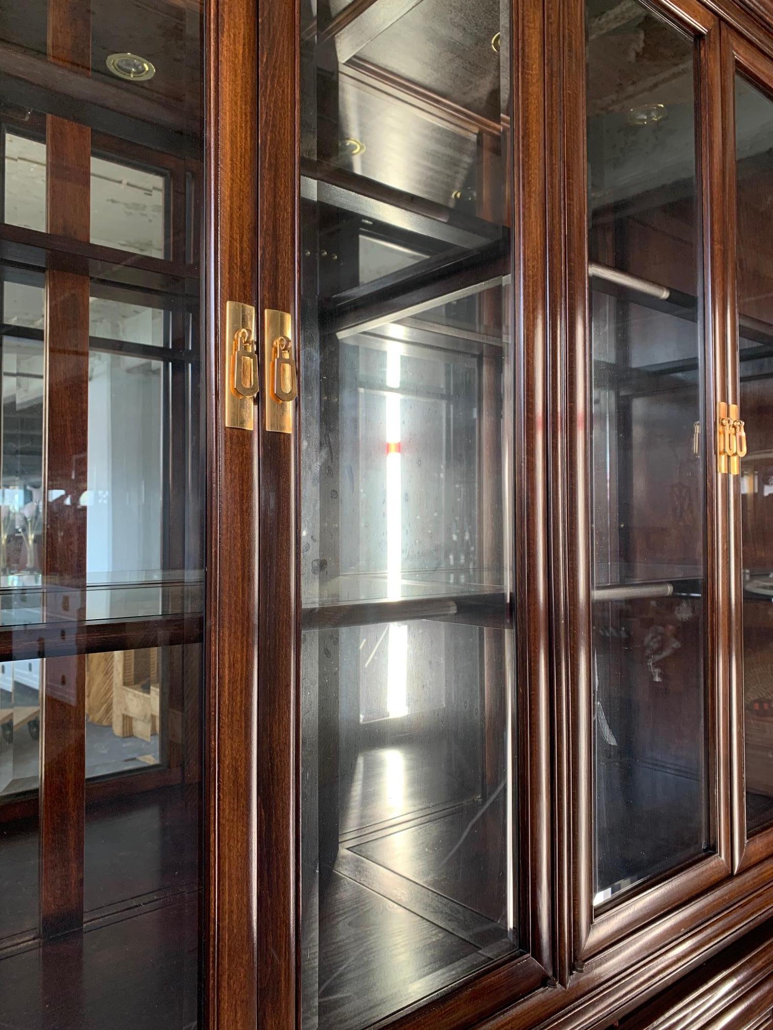 Die asiatische Chinoiserie-Vitrine ist aus massivem Rotholz gefertigt und mit Messingbeschlägen versehen. Beleuchteter Innenraum mit verspiegelter Rückseite und Glasböden. Handgeschnitzte Schubladengriffe und Türblätter. Insgesamt sehr guter Zustand.