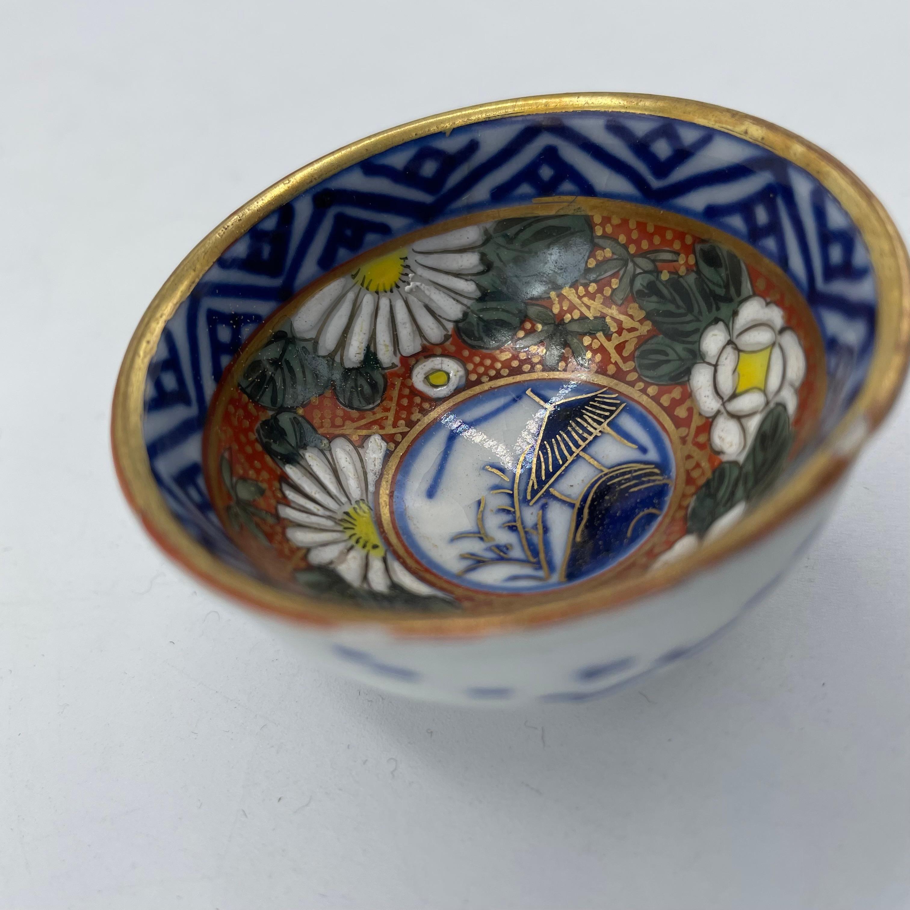 This is a small cup for drinking sake. It is called Ochoko in Japanese.
It was made in showa era around 1970s.  It is made with porcelain and all hand painted. 
This is Kutani ware.
Design is with some Chrysanthemums and a landscape.

On the bottom
