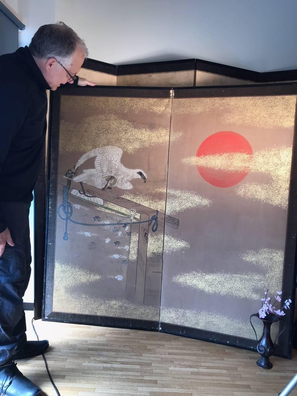 Japan, a fine two-panel screen Byobu of a tethered and perched prized falcon / hunting bird rendered in white gofun and intently stairing beyond a brilliant orange sun all surrounded by generous gold mist fleck clouds and original silk brocade from