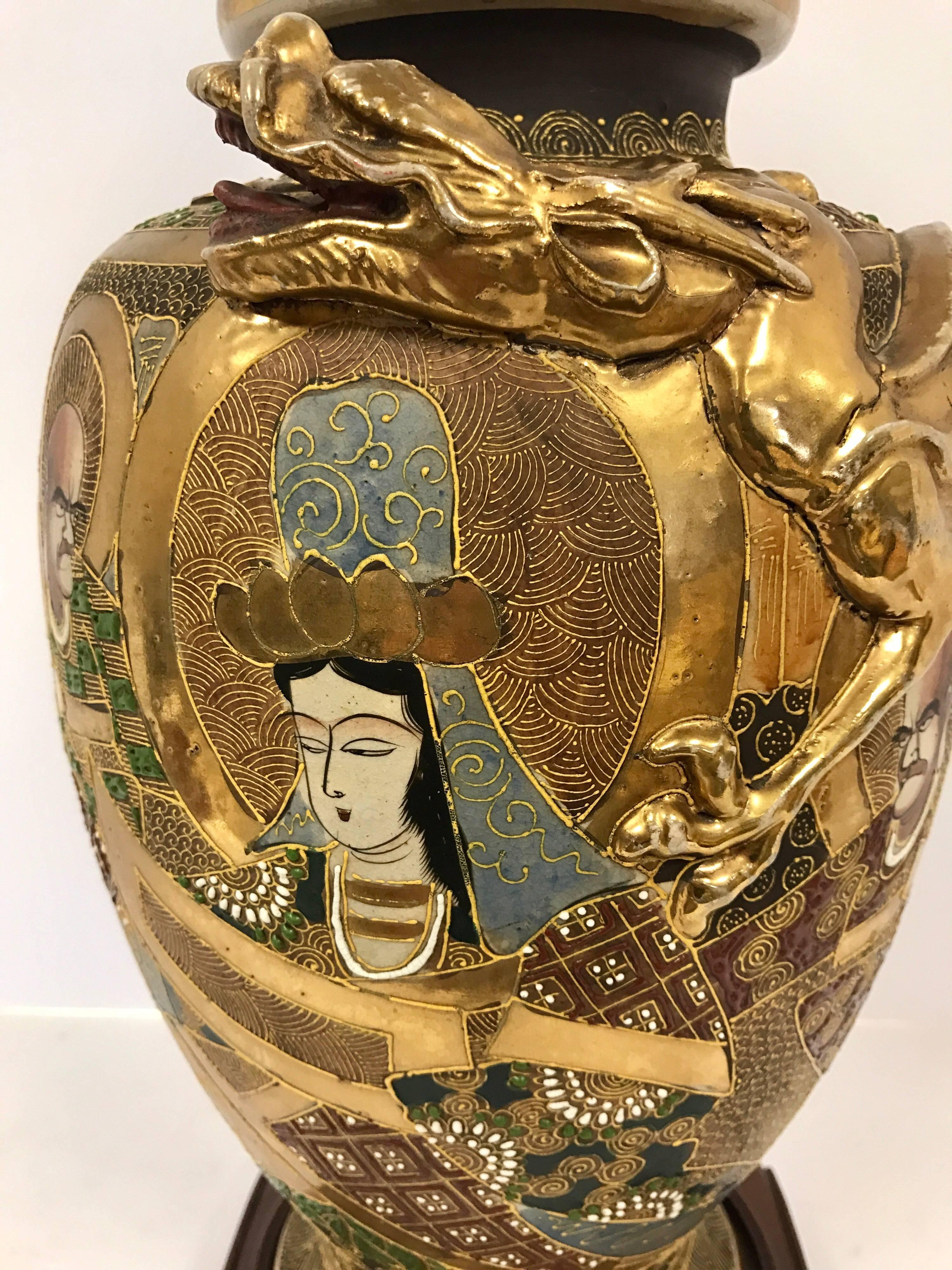 Elegant gold gilt Japanese Satsuma urn dragon lamp with raised figures. Base is elegant curved mahogany wood. Wired for USA and in working order.