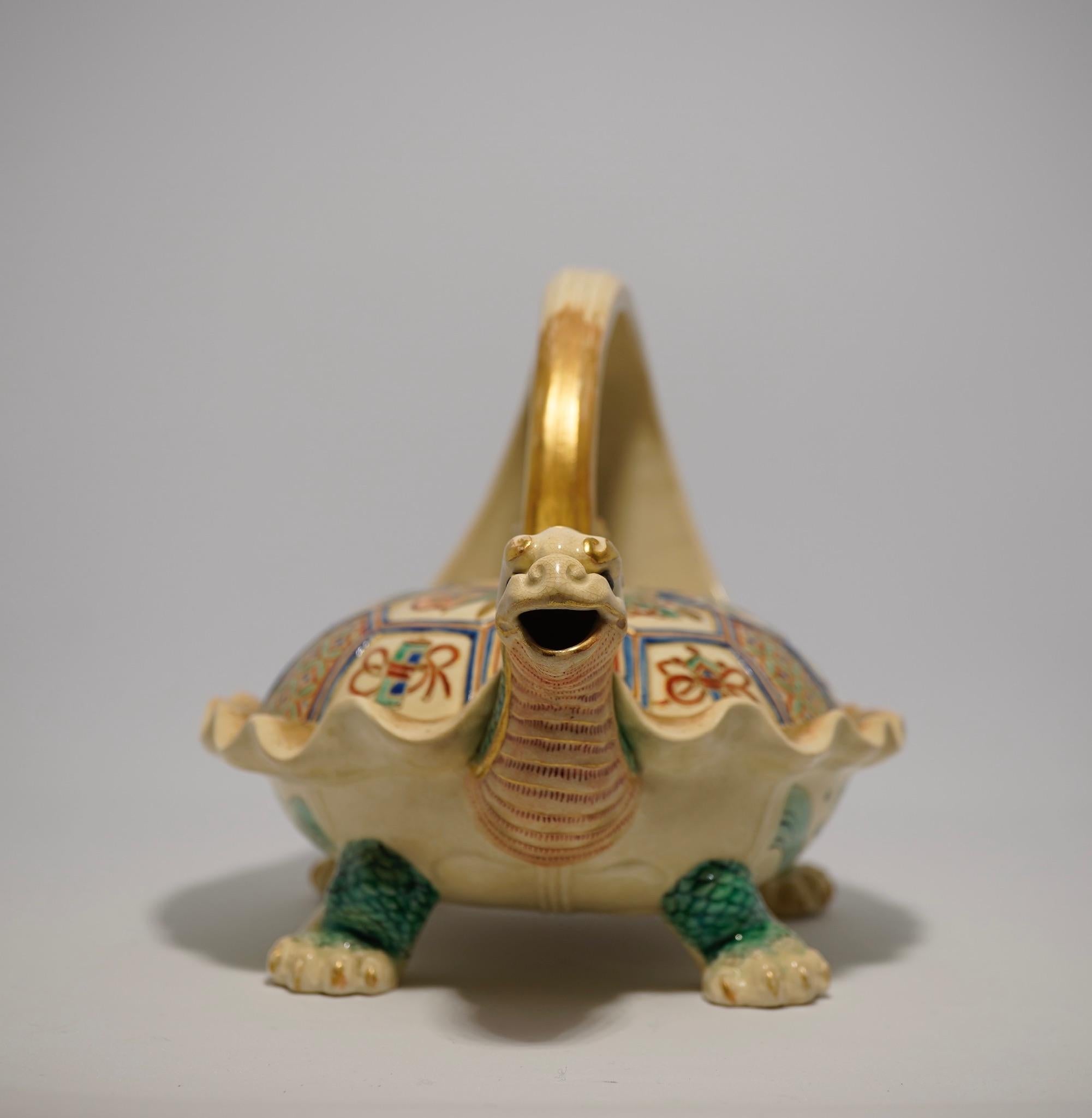 Satsuma style tea kettle, in the form of a mythical Minogame (ancient turtle) standing four-square on short feet, the shell segments brightly decorated with patterns, precious objects, and flowers, the lid bearing a tiny offspring, a large curling