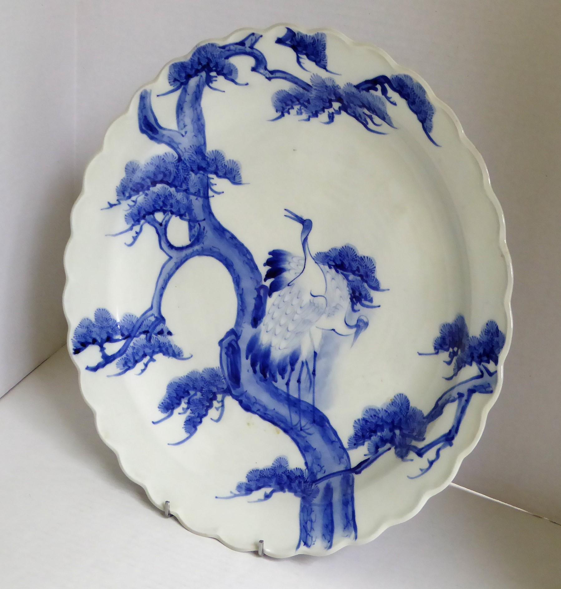 Beautiful Meiji Period blue and white Japanese Imari charger depicting a standing pair of cranes or storks on pine tree. The back has stylized depictions of waves. Appropriate firing marks centered on back and Japanese stamp Aoki Brothers of Arita.