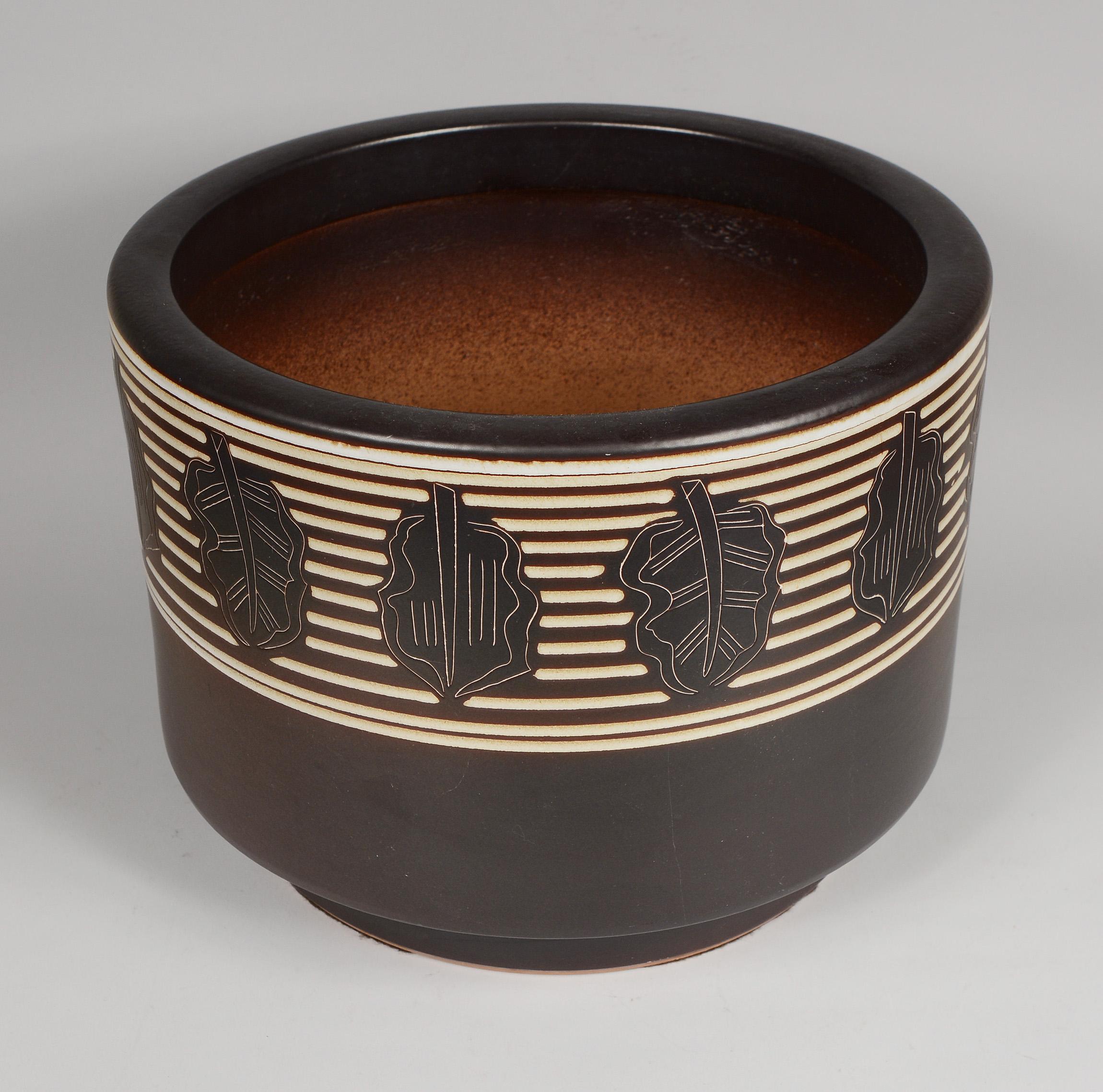 Large planter by the Otagiri Mercantile Company. Otagiri was headquartered in San Francisco and their products were made in Japan. This has a dark brown glaze with incised leaves and rings. The top edge of the planter is rolled. This is in good
