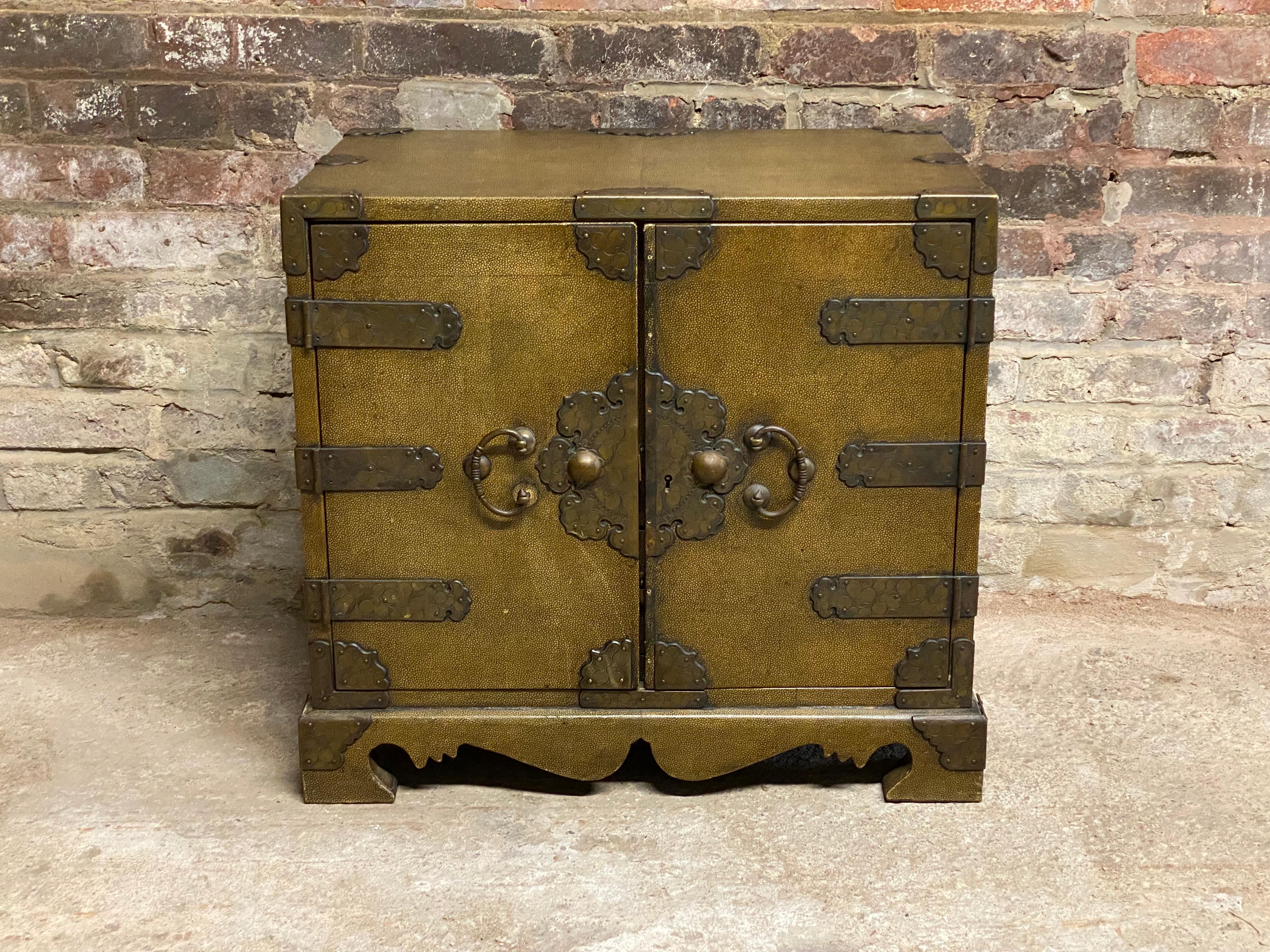 Japanese shagreen clad mini tansu. Beautifully cast and engraved floral and scrolled hardware, hinges and mounts. Block front cabinet with two doors and five interior drawers supported by a sinuous scrolled base. The interior drawers are painted