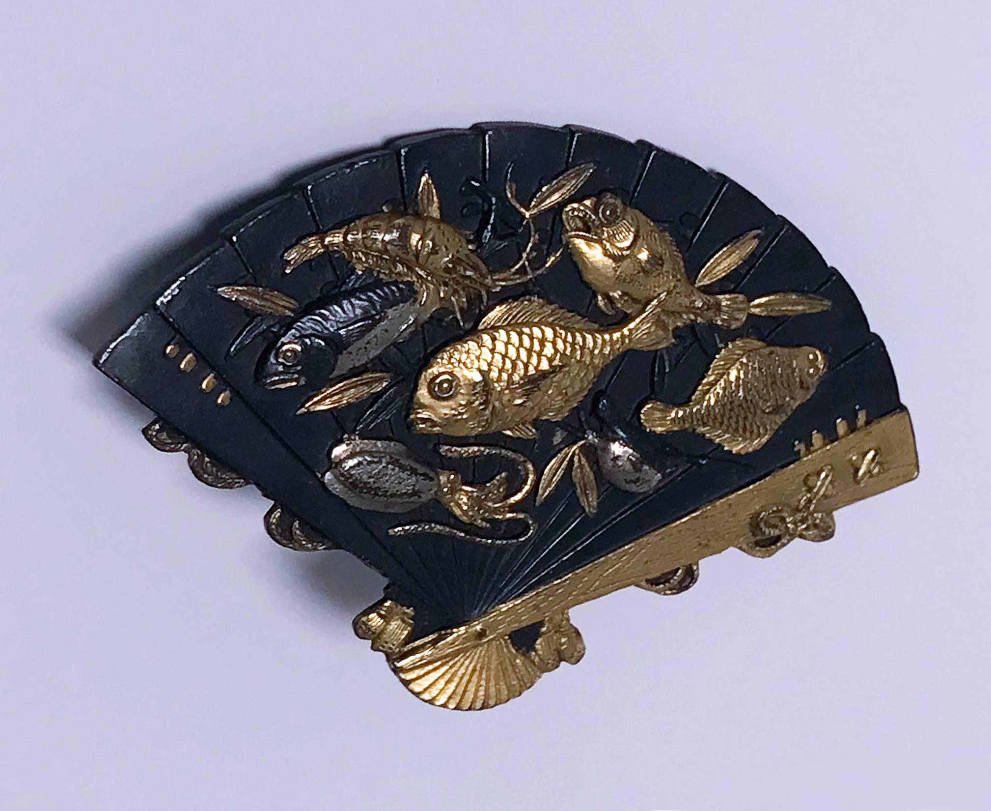 Antique 19th century Japanese Shakudo Fan Brooch, C.1880. The brooch depicting swimming fish inlaid with contrasting gold and silver on blackened copper, framed by fan's decorations. The miniature details of fish, branches and flowers show highly