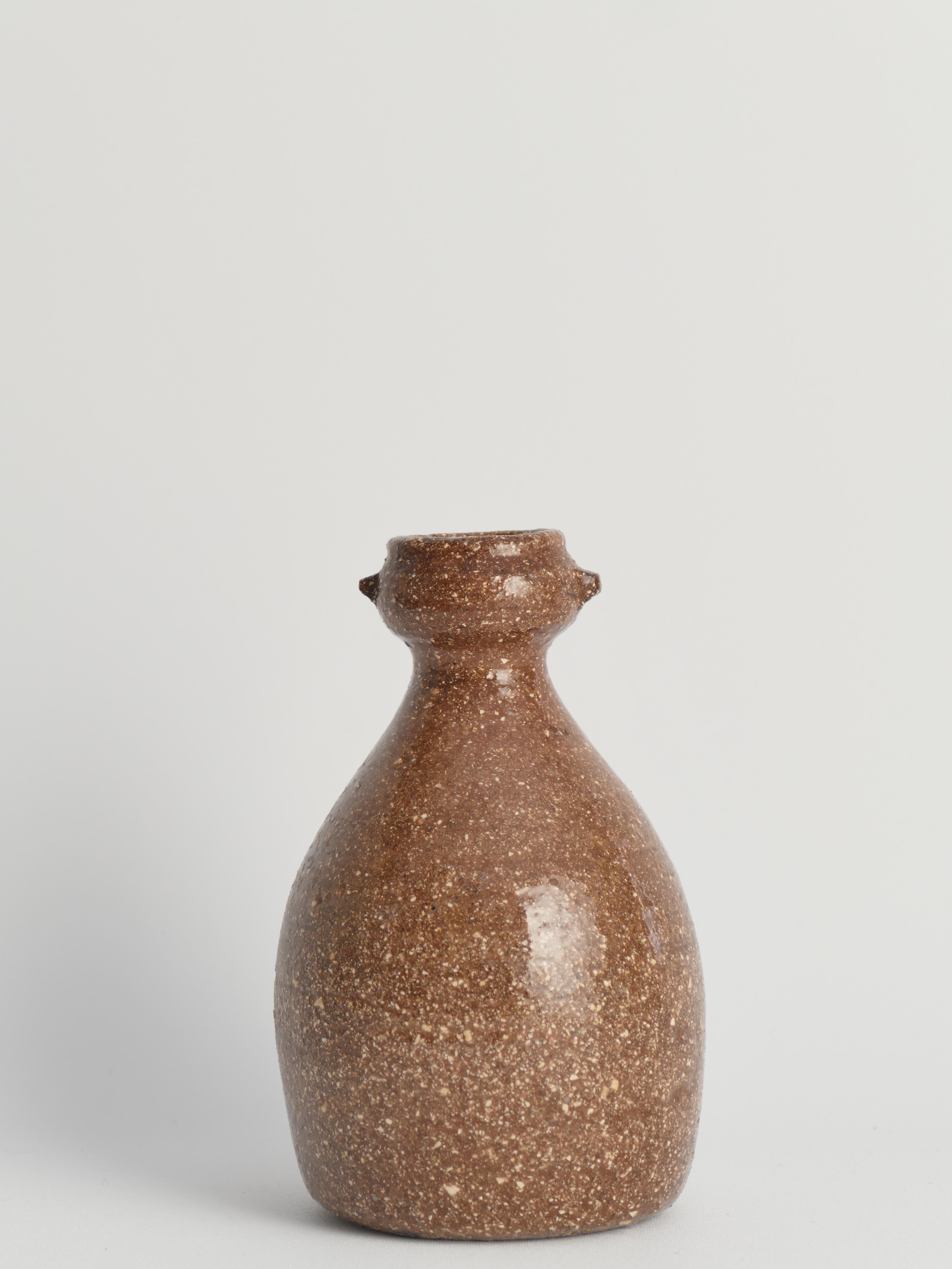 This exquisite handmade stoneware vase is reminiscent of the famed Japanese Shigaraki pottery tradition, renowned for its use of local sandy clay from the bed of Lake Biwa, imparting a warm orange hue and exceptional durability to the