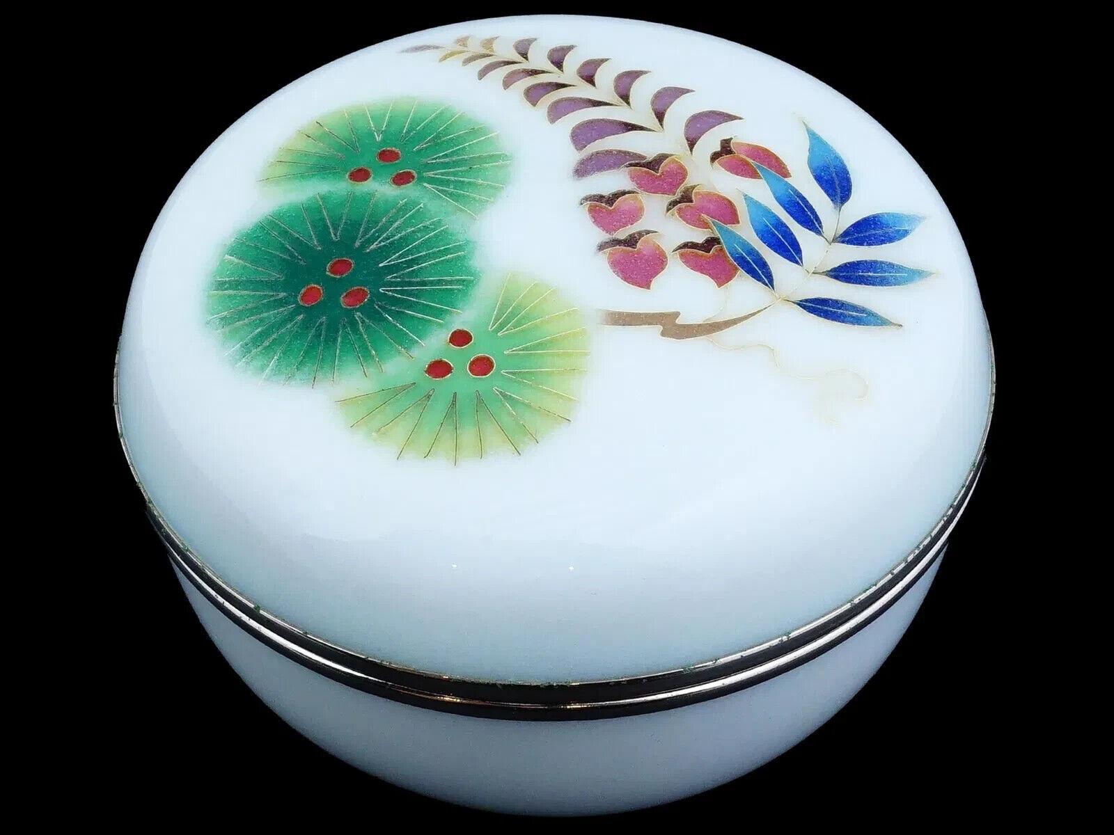 Caja esférica con tapa de esmalte cloisonné japonés, fabricada por la empresa Ando. Periodo Showa, de 1926 a 1989. La caja está decorada con esmalte blanco lechoso en toda su superficie y con un motivo floral de esmalte cloisonné en colores azul,