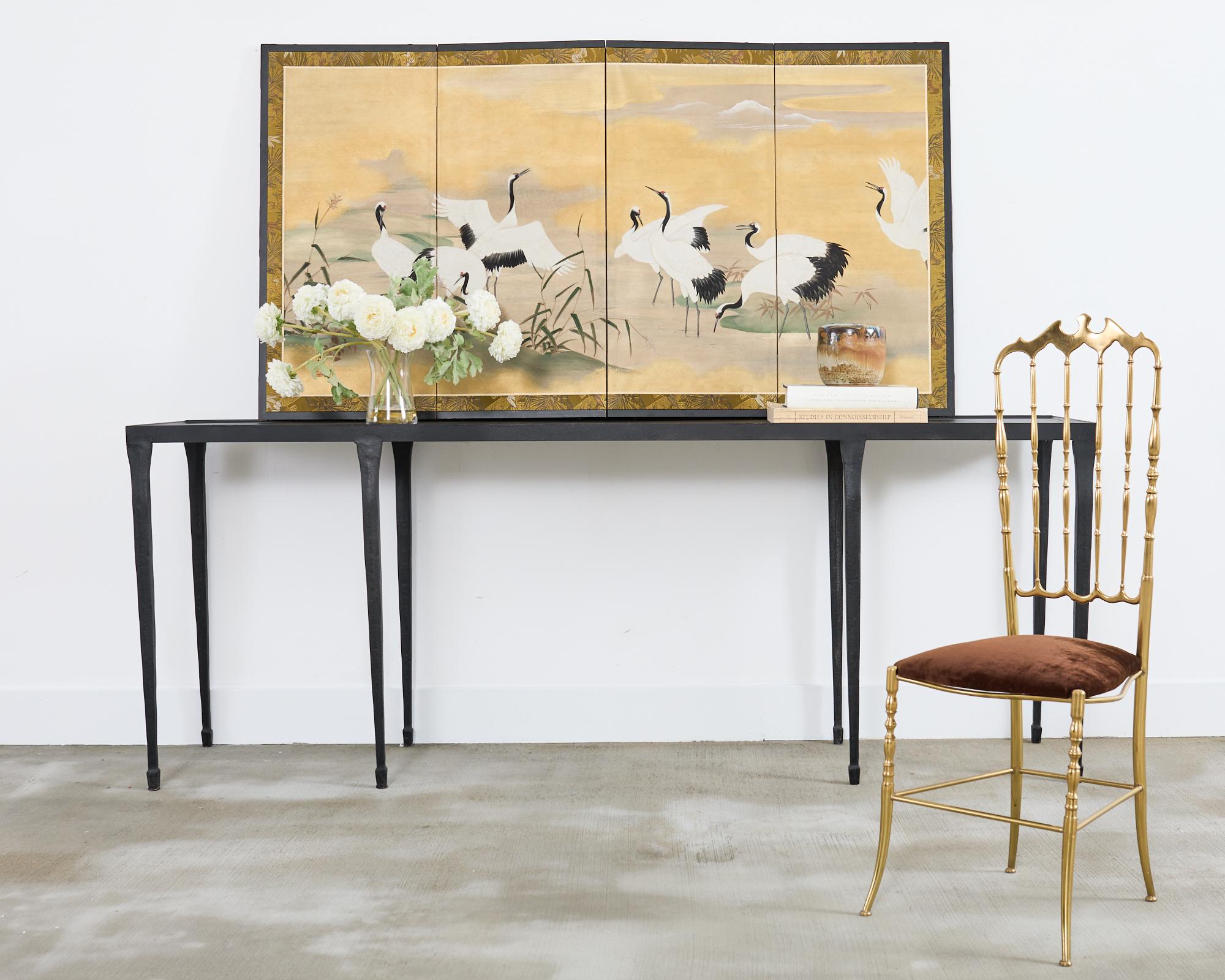 Exceptional Japanese Showa period four-panel byobu screen depicting eight white Manchurian cranes feeding along a meandering stream. The screen features vibrant ink and color natural pigments over a dramatic radiant gilt background. Intricate