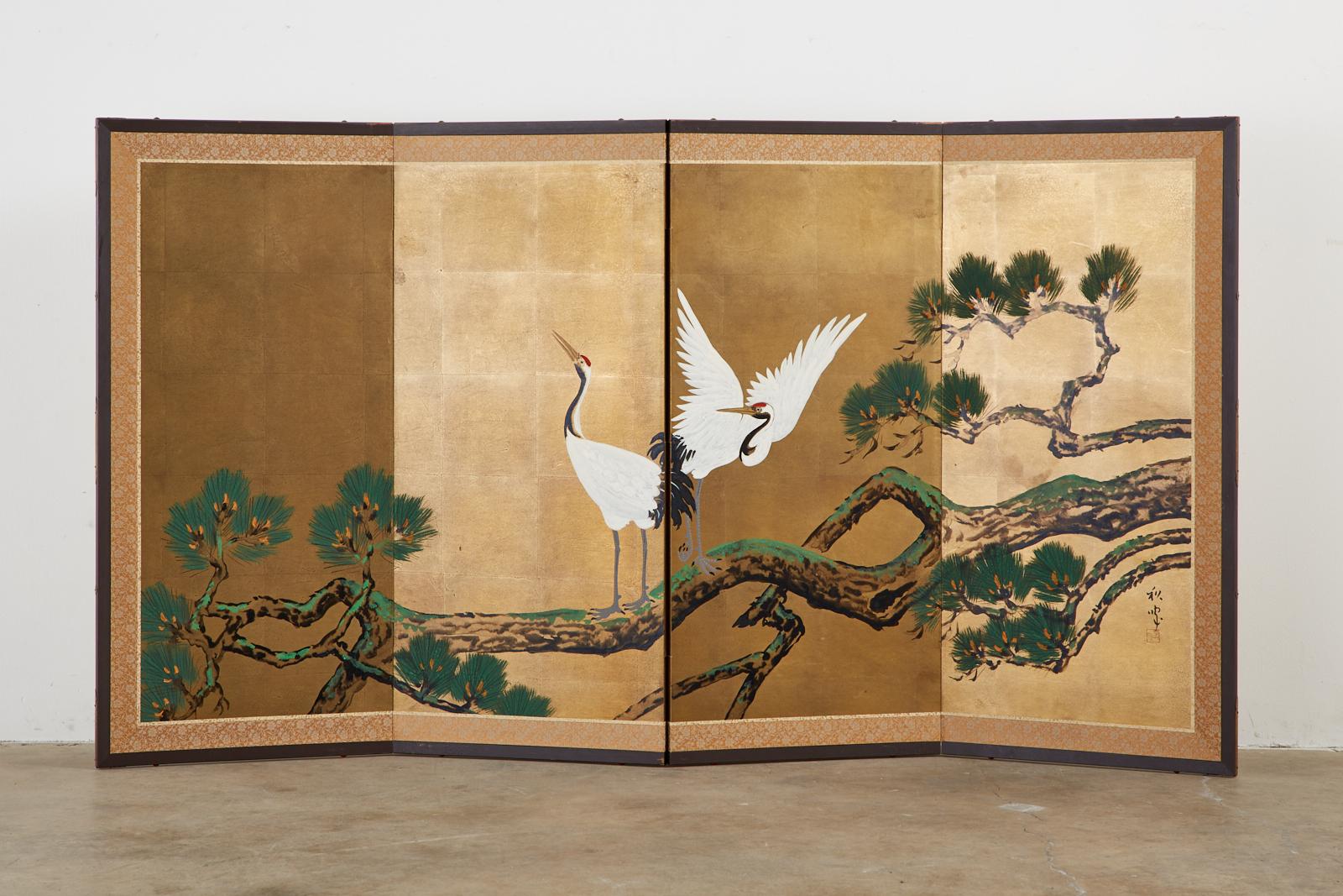 Colorful Japanese Showa period four-panel folding screen depicting a pair of Manchurian red-crowned cranes perched in a pine tree. Crafted on a dramatic gilt square background with ink and color pigments. Set in a lacquered wood frame with a silk