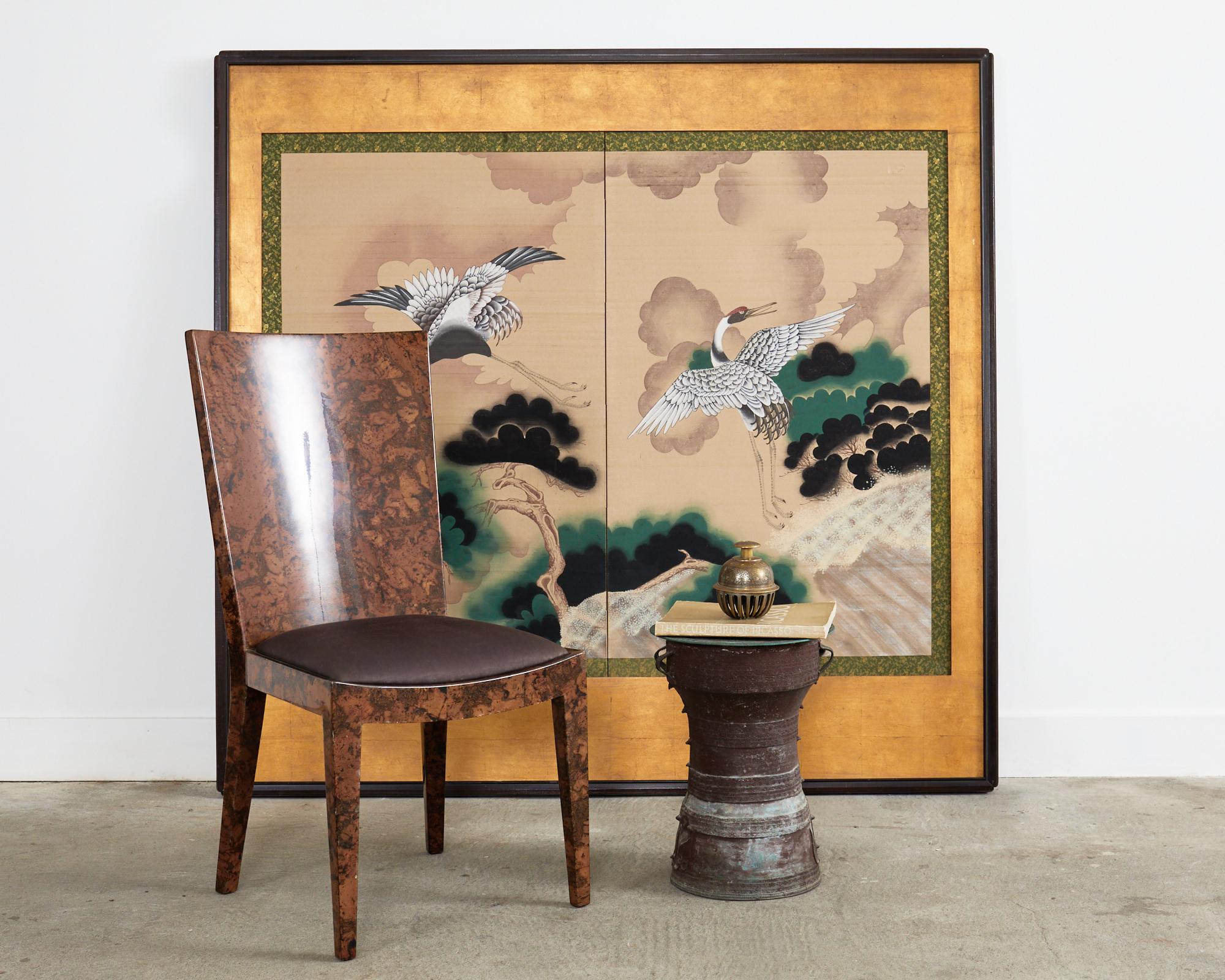 Imposing Japanese Showa period two panel byobu screen later mounted in a large gilt and ebonized wood frame. The screen depicts a pair of large redheaded Manchurian cranes flying amid the stylized pine trees and clouds. Ink and natural color